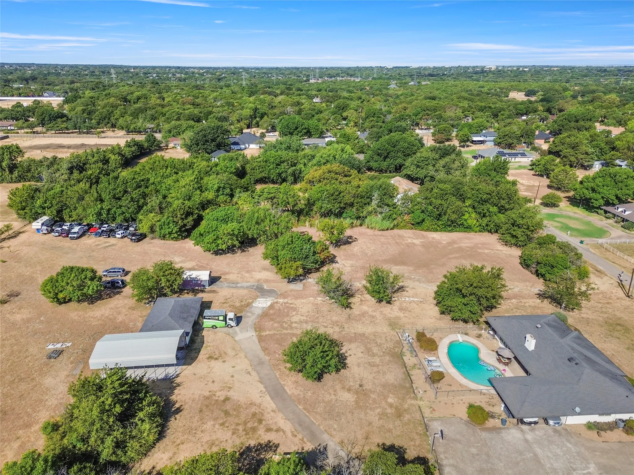 Expansive property featuring a main residence with a swimming pool, a separate outbuilding with a metal roof, and mature trees