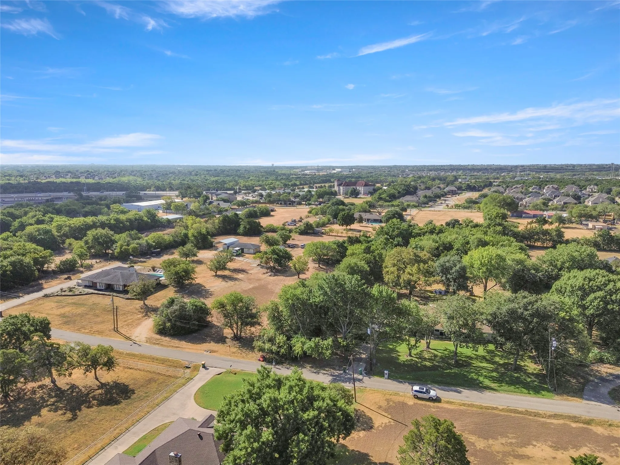 Expansive property featuring mature trees and open land, with a paved road visible