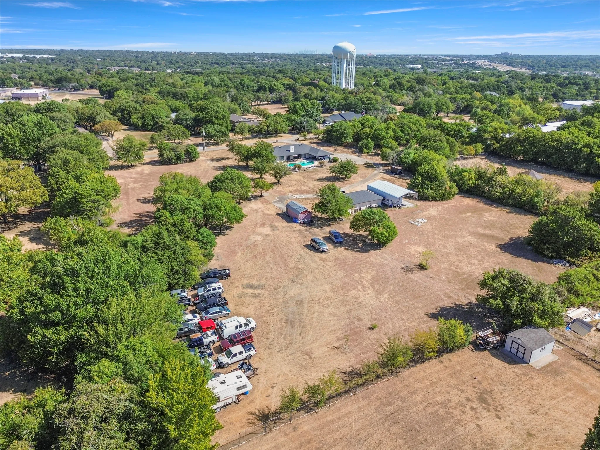Expansive property with mature trees, a detached storage building, and a water tower structure in the background