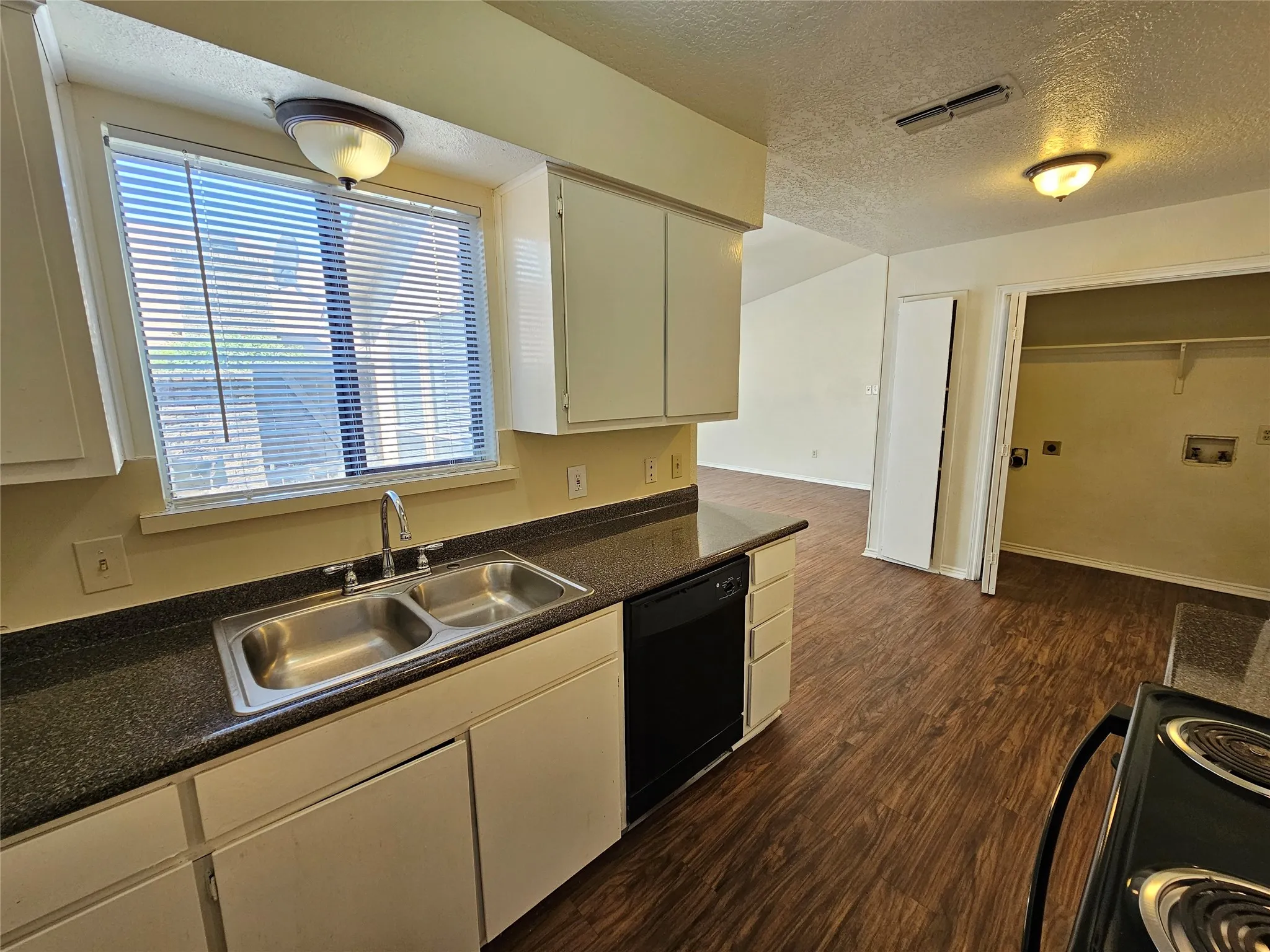 Kitchen featuring wood-finish flooring, white cabinetry, dark countertops, and a double-basin stainless steel sink
