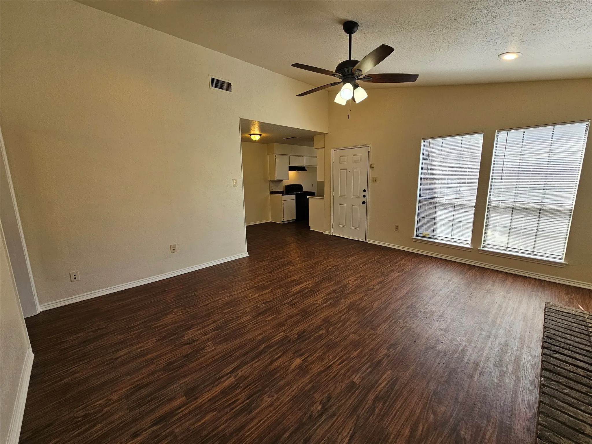Vaulted ceiling with a ceiling fan, wood-finish flooring, and multiple windows with blinds