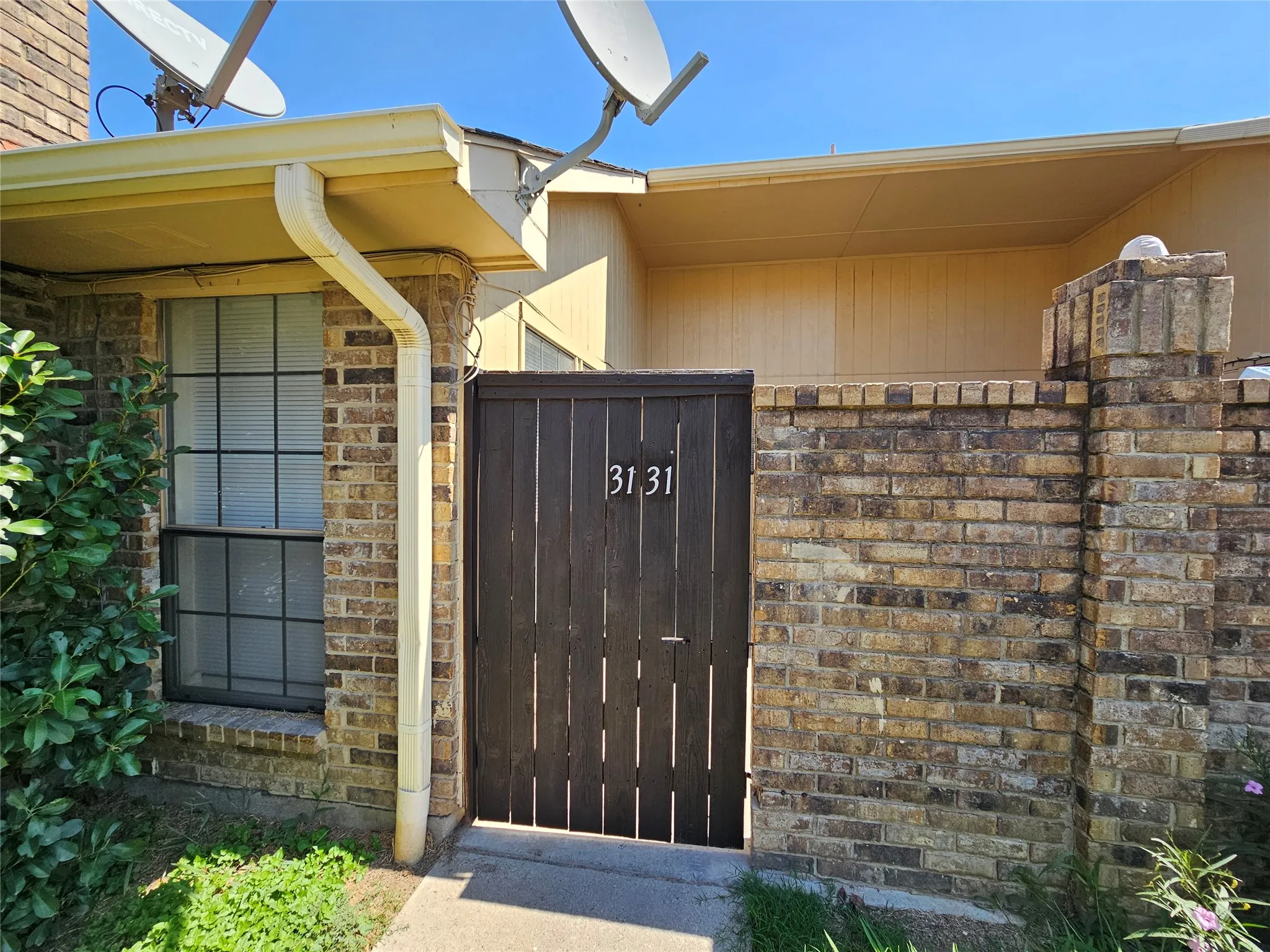 Brick facade, dark wood-finish gate, gated entry, window with gridded panes, rain gutter system