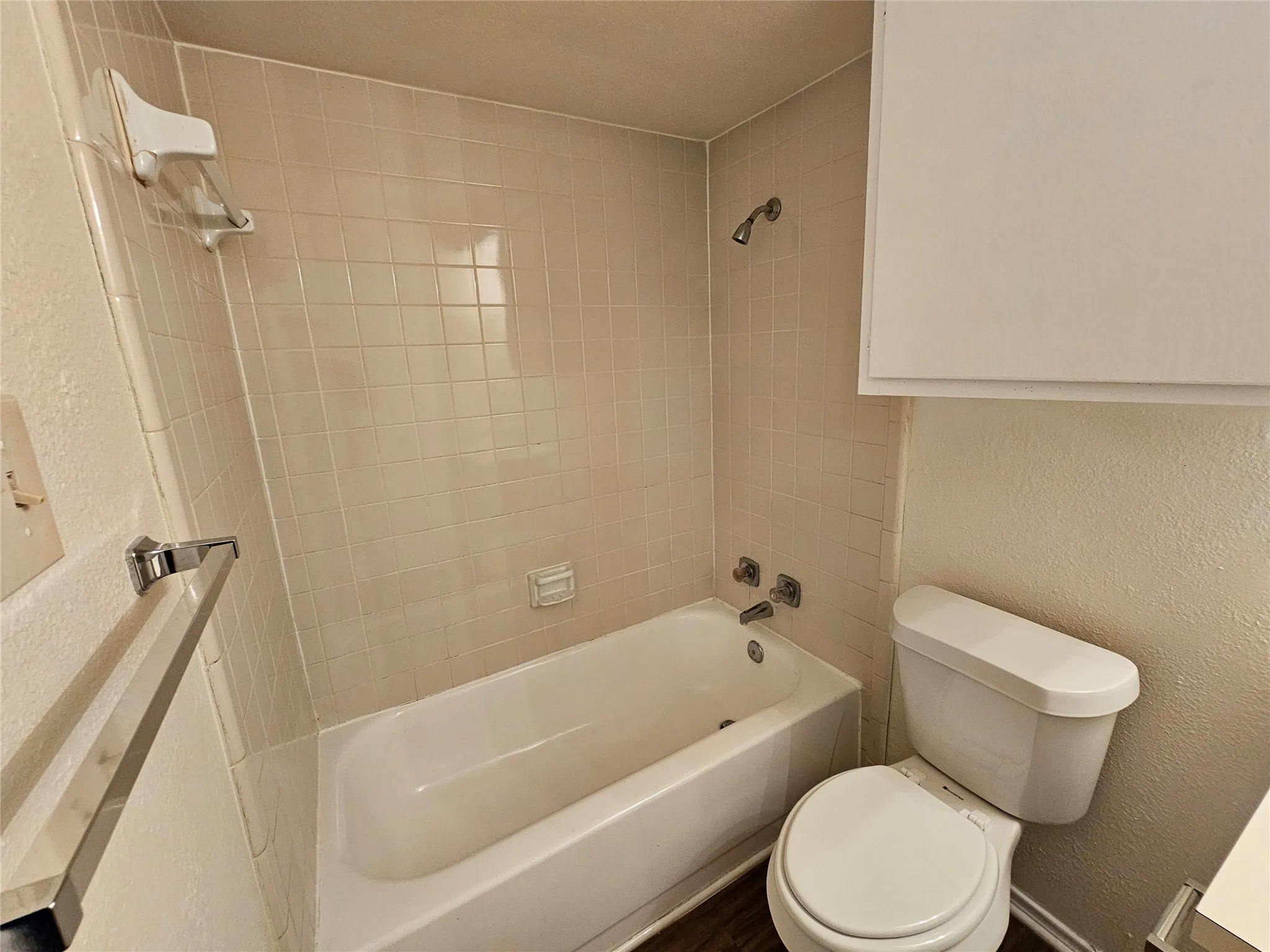 Bathtub with tiled surround, shower fixture, and wall-mounted storage cabinet