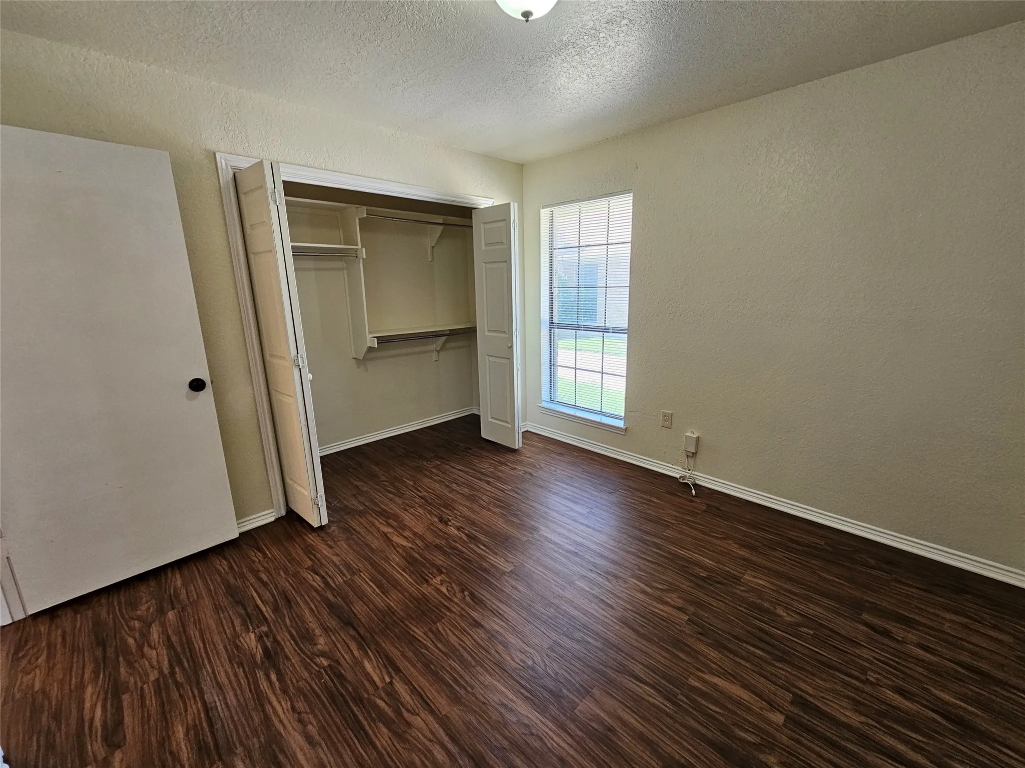 Wood-finish flooring throughout, light-toned walls, built-in closet with shelving and hanging rods, and a multi-pane window