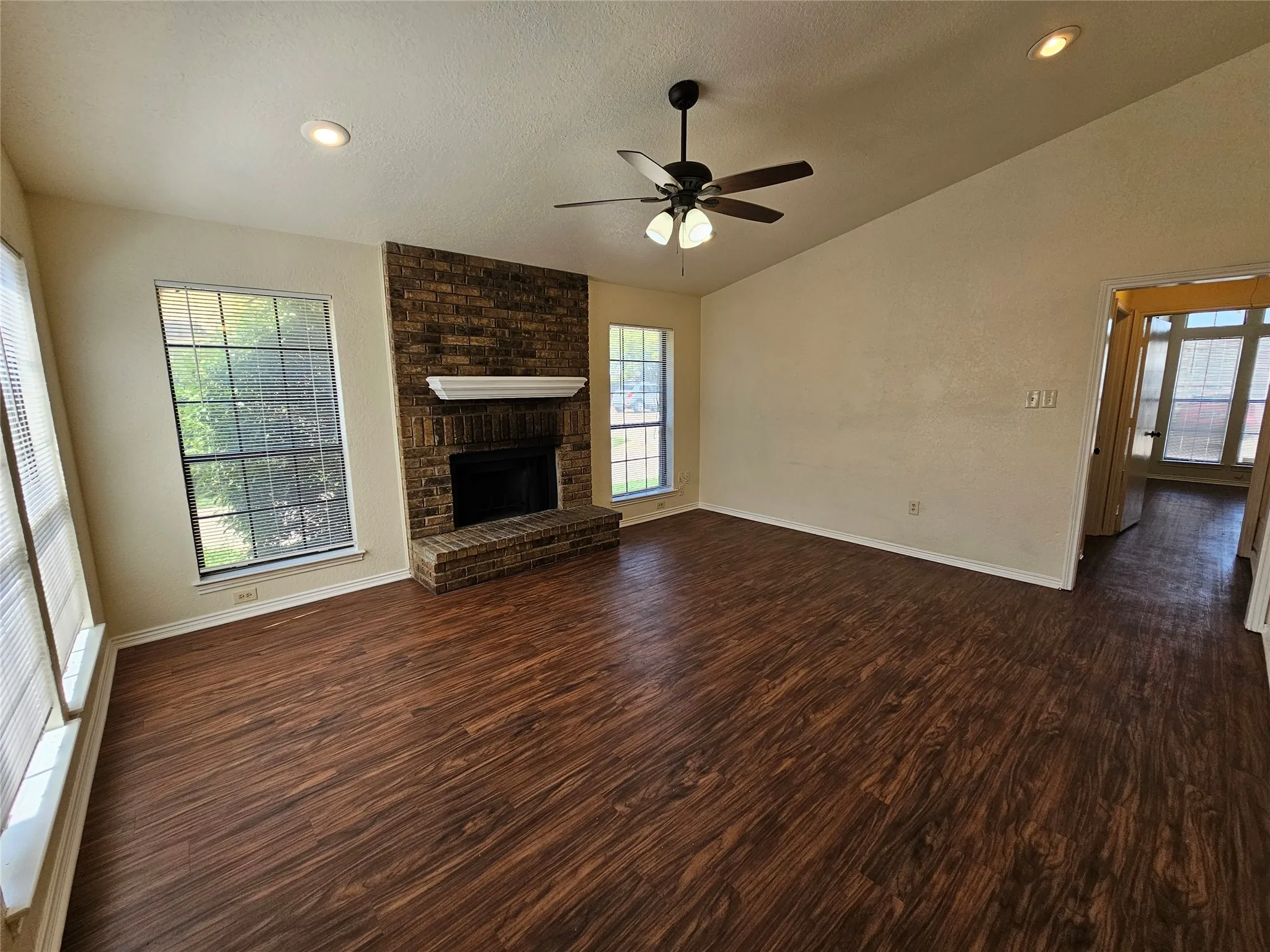 Vaulted ceiling with a ceiling fan, recessed lighting, wood-finish flooring, and a brick fireplace with a white mantel