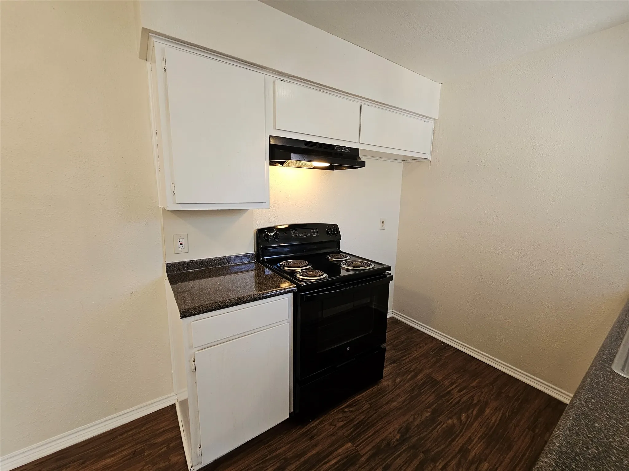 White upper and lower cabinetry, dark countertop, black electric range, and wood-finish flooring