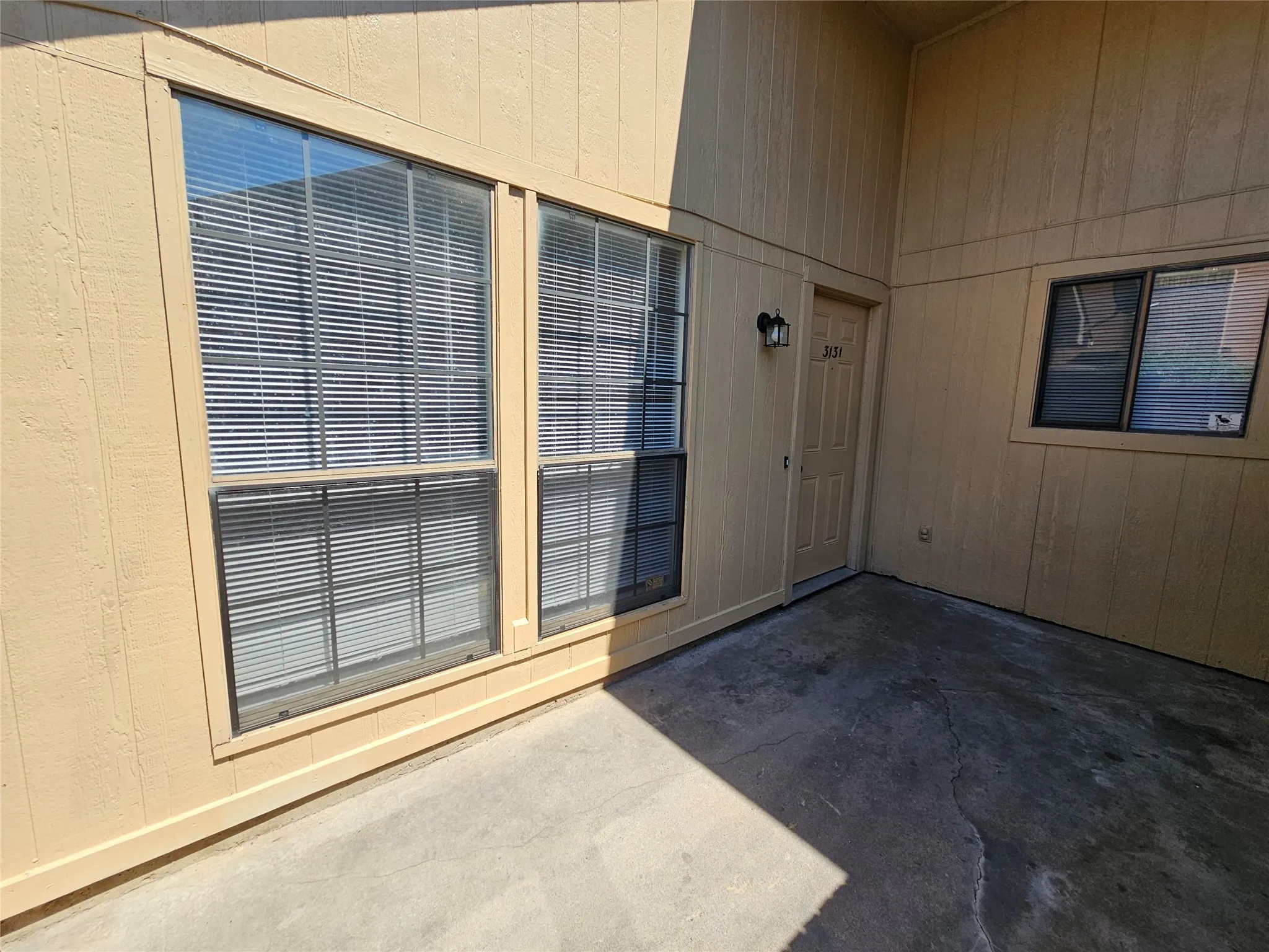 Covered patio with large sliding glass doors featuring horizontal blinds, wood-finish wall paneling, and concrete flooring