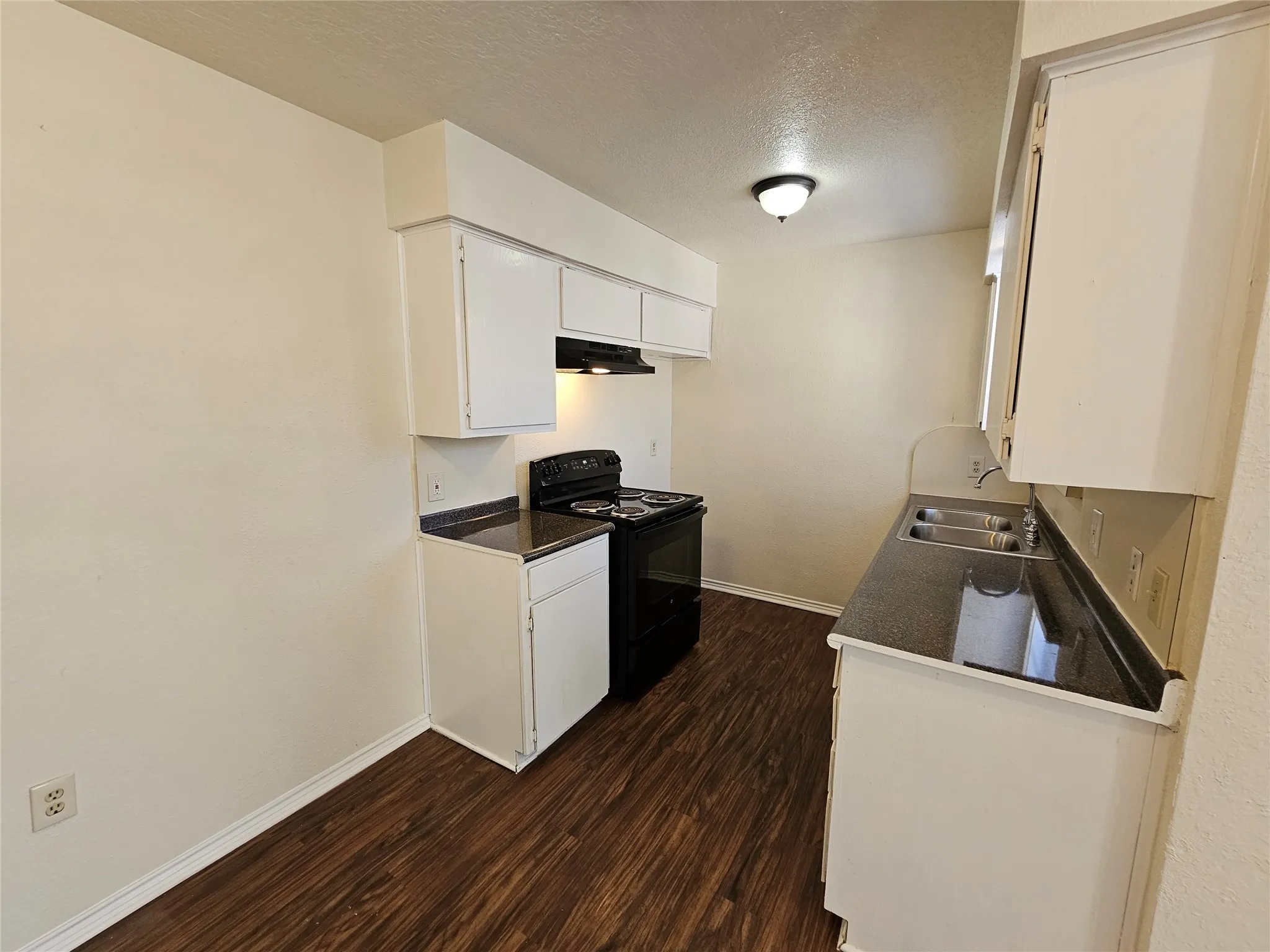 Kitchen with white cabinetry, dark countertops, a black range, and wood-finish flooring