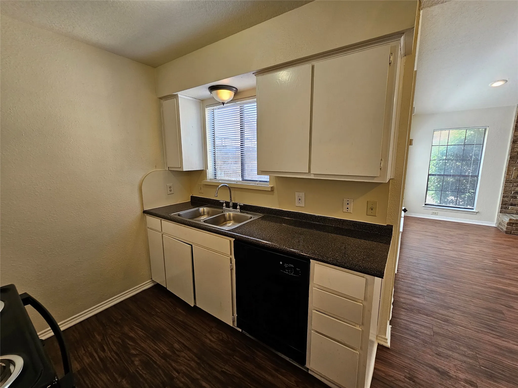 Kitchen featuring white cabinetry, double basin sink, dark countertop, and integrated dishwasher