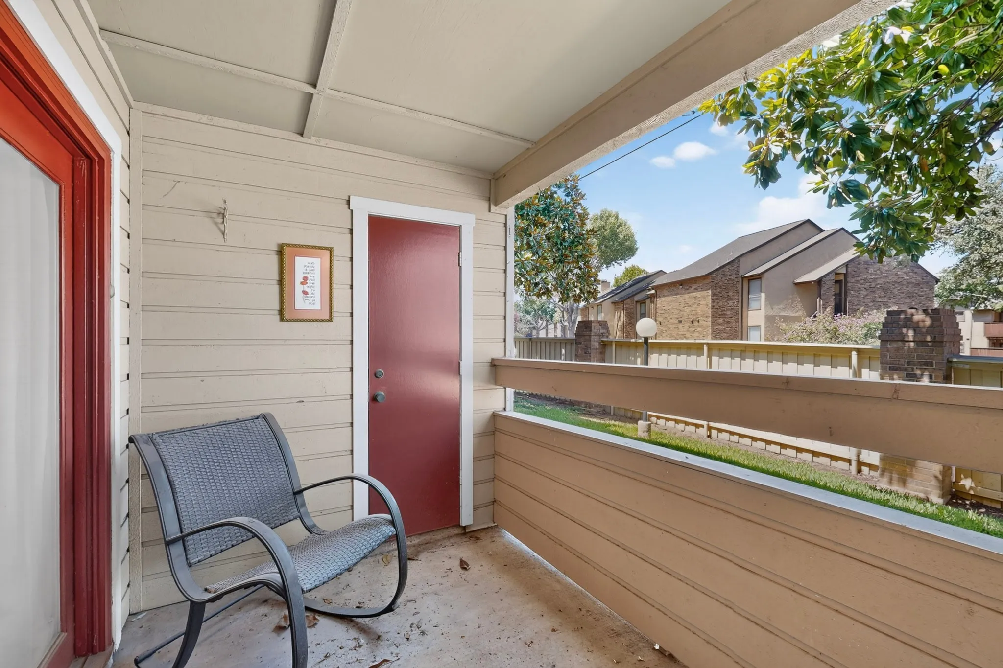 Covered outdoor balcony with concrete flooring, accented by a red-painted door and trim