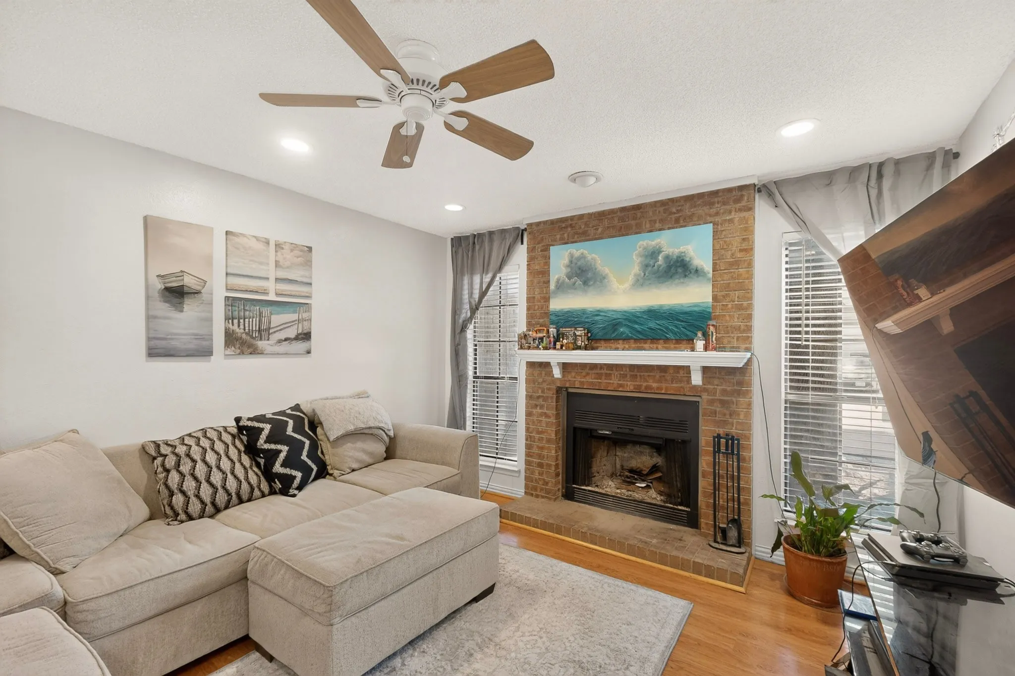 Fireplace with a brick surround and white mantel, wood-finish flooring, recessed lighting, and a ceiling fan with wood-finish blades