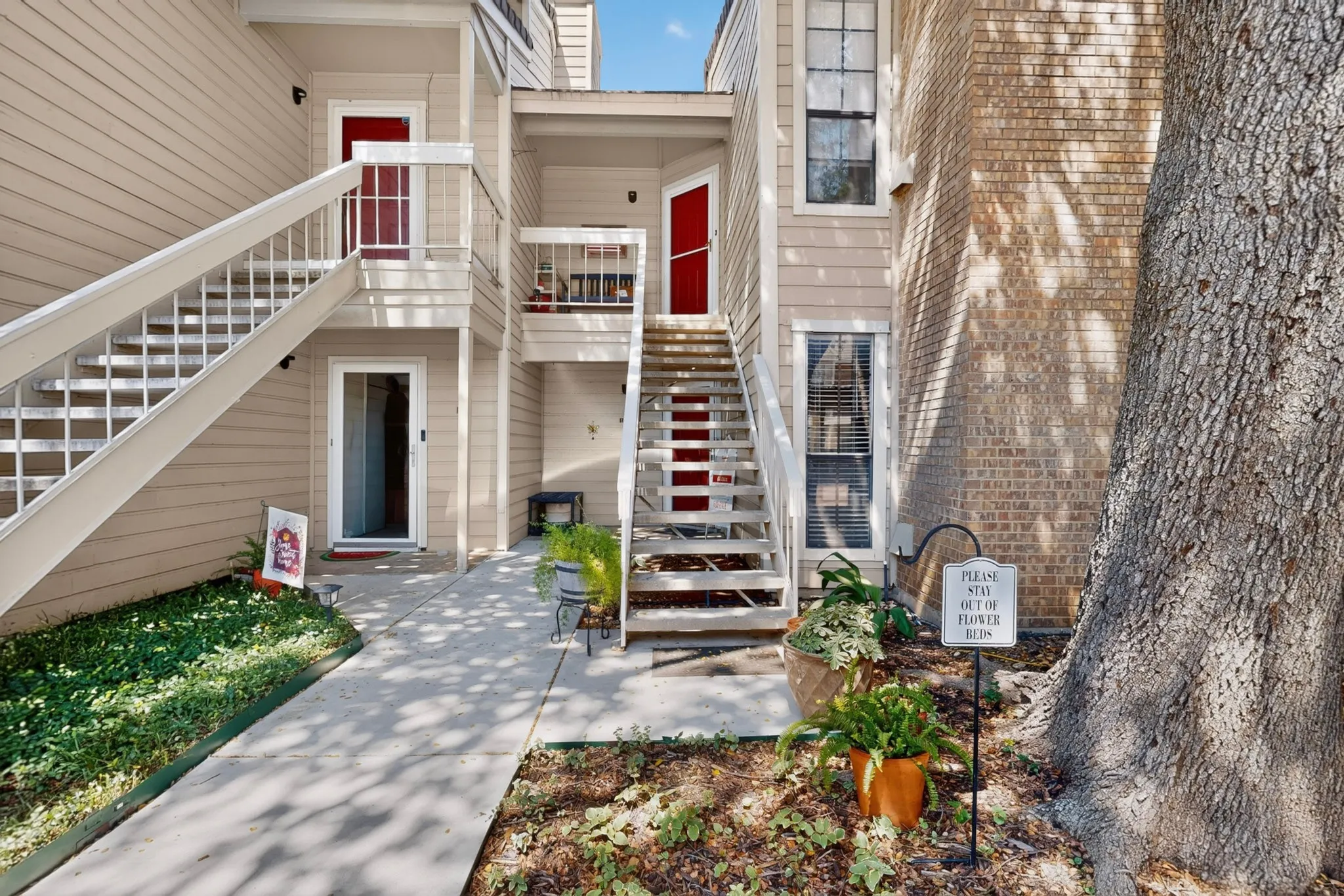 Multi-level residential building featuring tan siding and exposed brick, with red entry doors and white exterior staircases