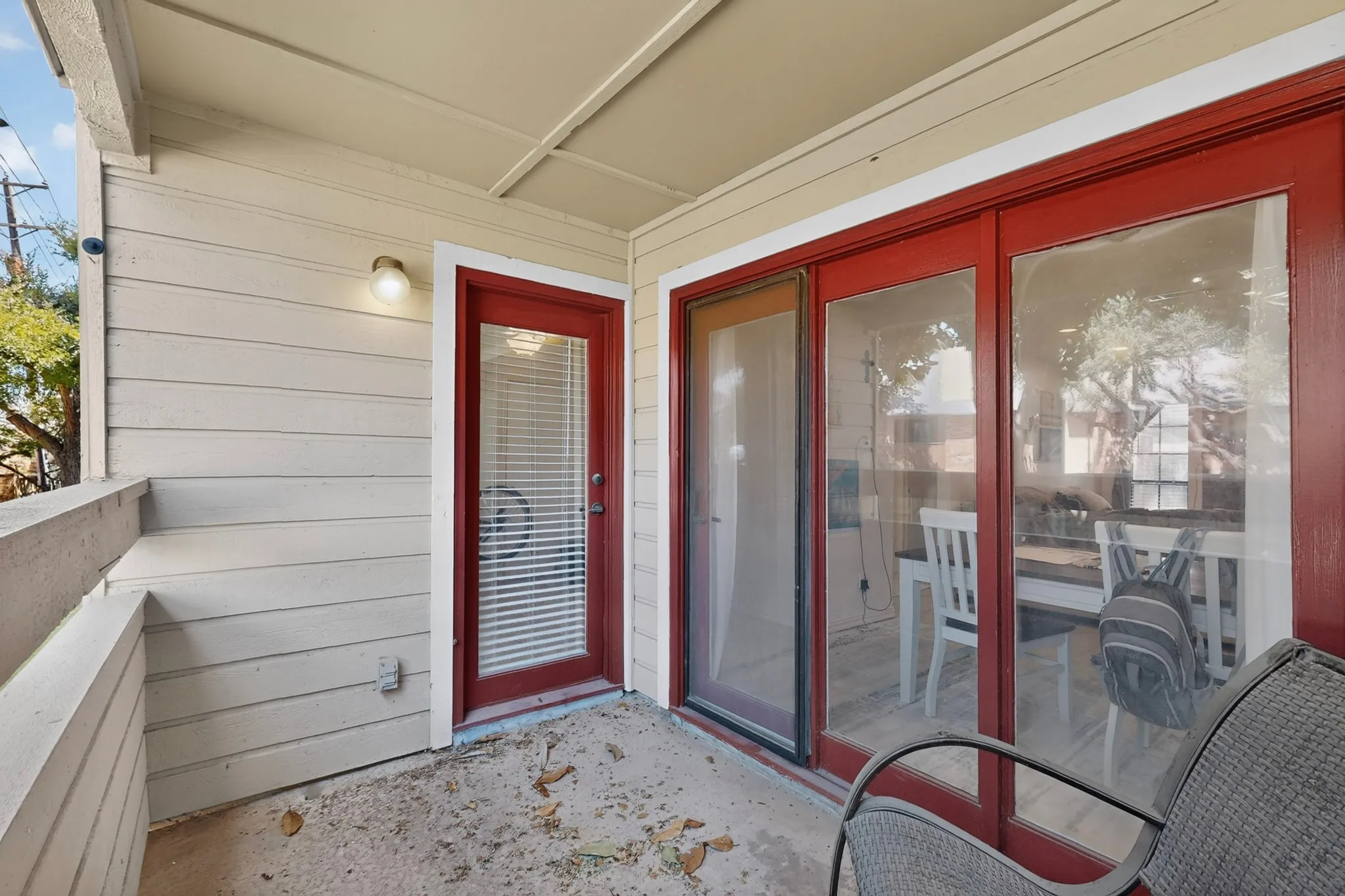 Covered outdoor patio with a concrete surface, red-framed glass-paneled door, and red-framed glass sliding doors
