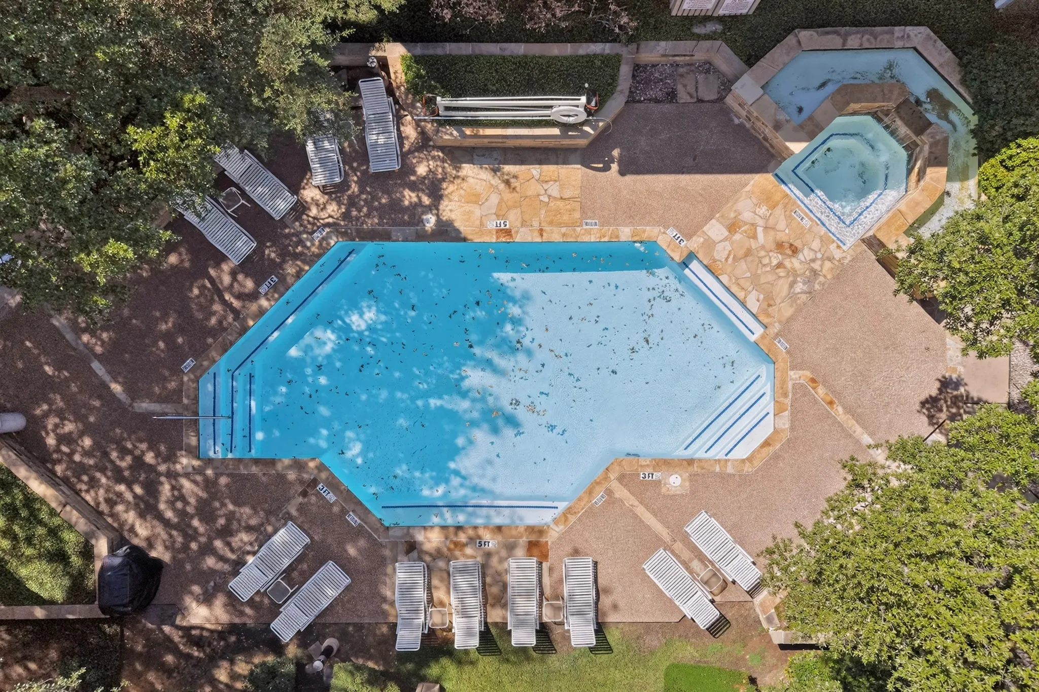 Outdoor swimming pool with integrated steps, adjacent hot tub, and stone-finish patio areas