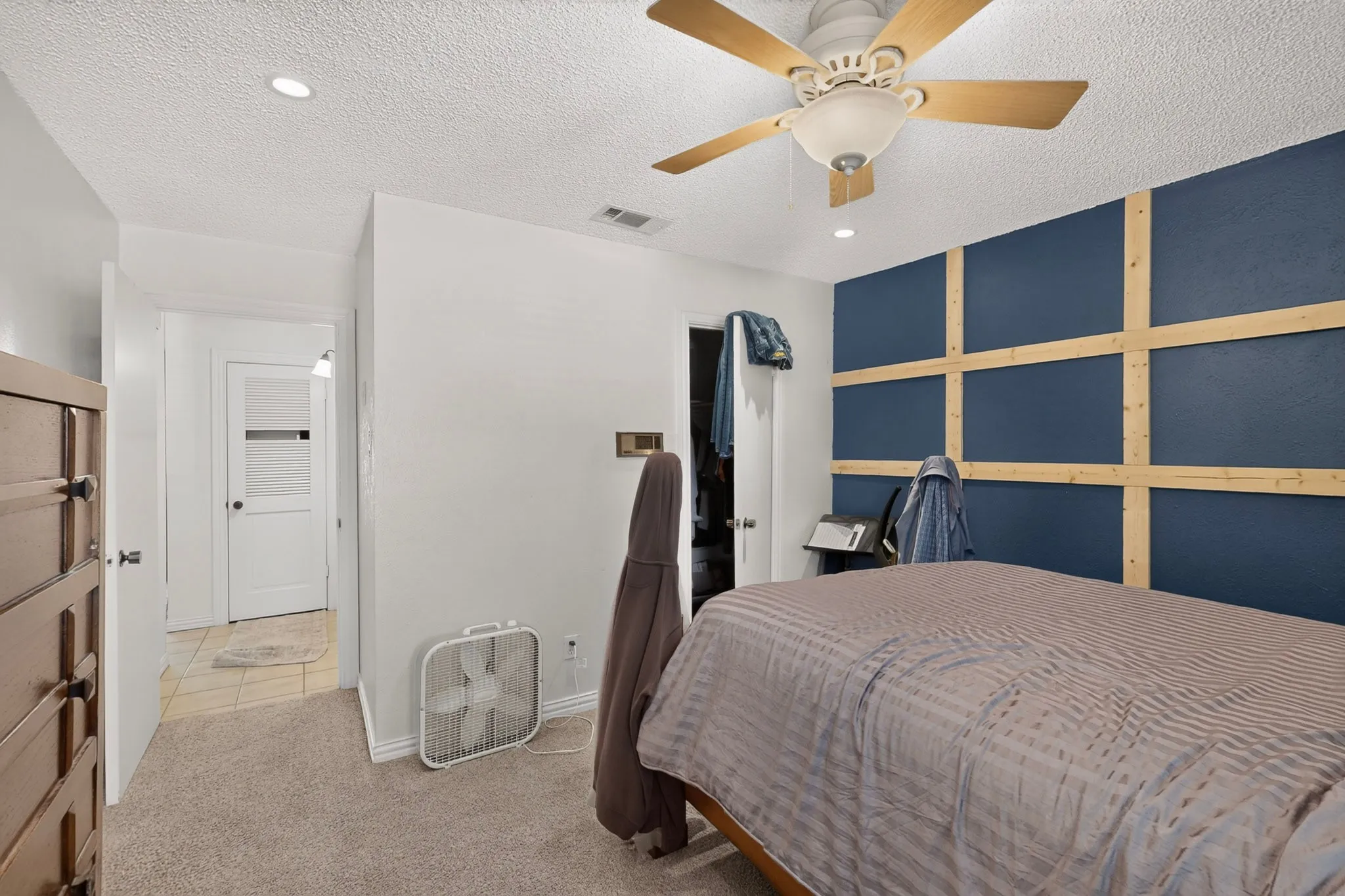 Recessed ceiling lighting, ceiling fan with wood-finish blades, accent wall with wood grid detailing, white interior door, and carpeted flooring
