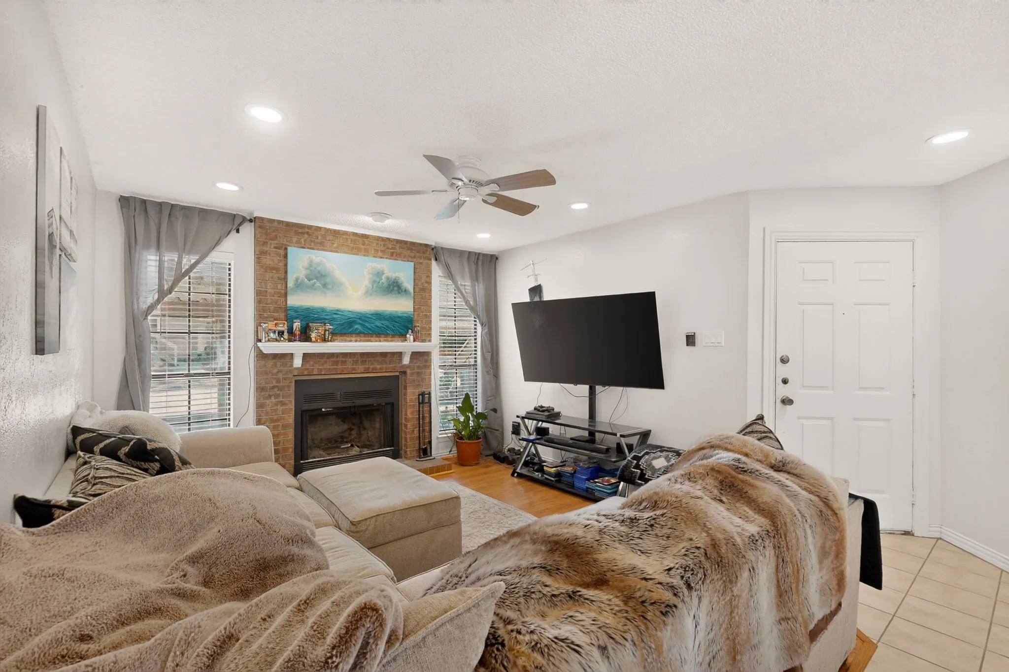 Inviting living room featuring a brick fireplace with white mantel, recessed lighting, ceiling fan, and abundant natural light.