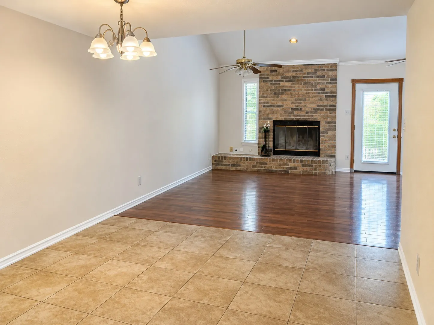 203- Tiled flooring, wood-finish flooring, brick fireplace with hearth, vaulted ceiling, and an exterior door with louvered blinds