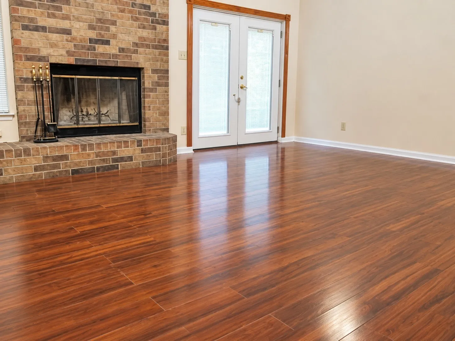 203- Wood-finish flooring throughout, brick fireplace with a raised hearth, and white French doors with transom windows