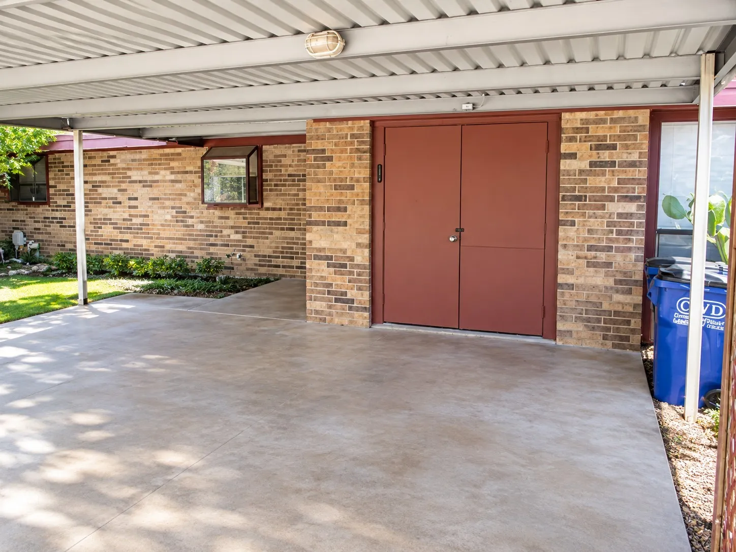 Covered carport with a concrete slab, brick exterior, and dual exterior doors