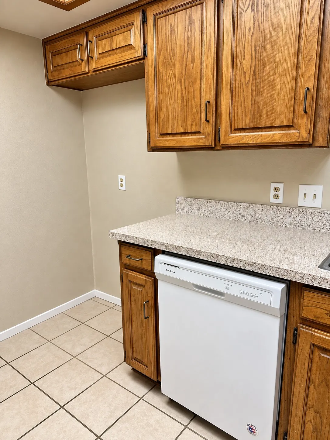 201- Built-in dishwasher, wood-finish cabinetry, tile flooring, and speckled countertop