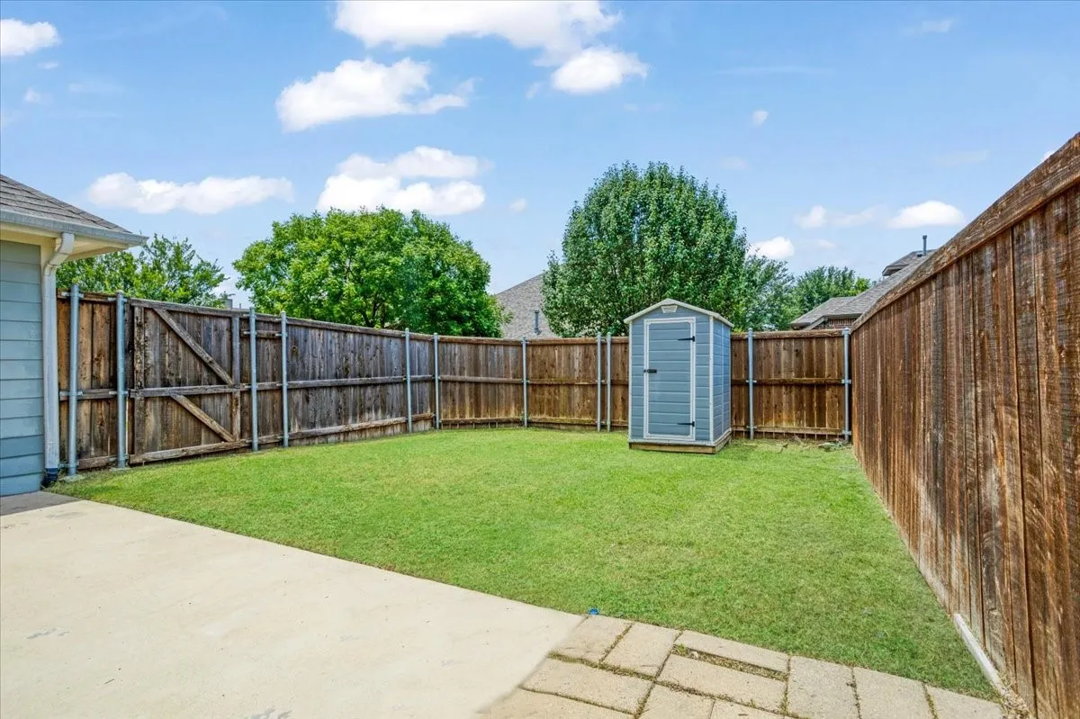 Fenced backyard featuring a manicured lawn, concrete patio, and a utility shed