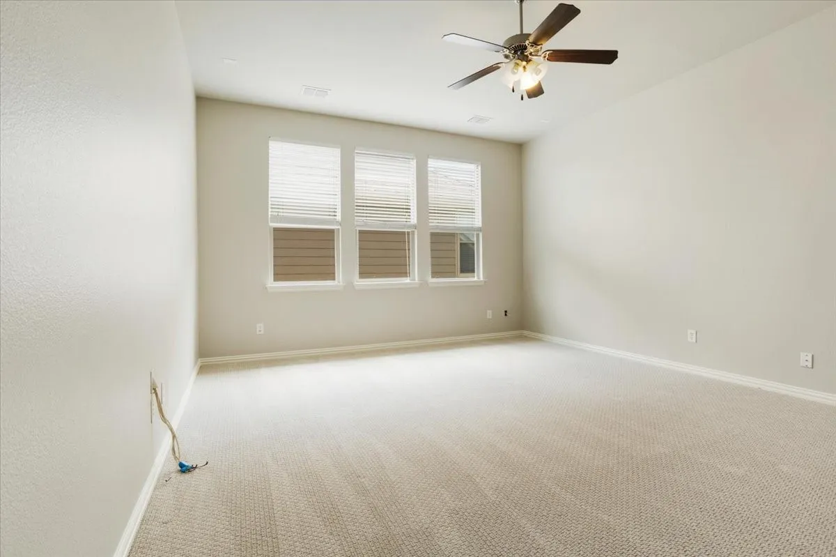 Vaulted ceiling with a ceiling fan, three windows with horizontal blinds, and neutral carpeting