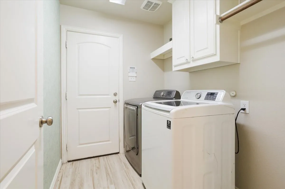 Laundry area featuring wood-finish flooring, white cabinetry, integrated shelving, and a clothing rod
