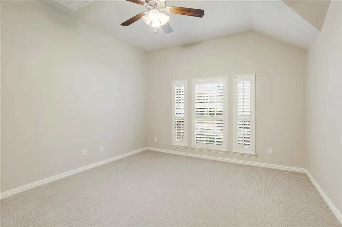 Vaulted ceiling with a ceiling fan, three windows featuring plantation shutters, and light-toned carpeting