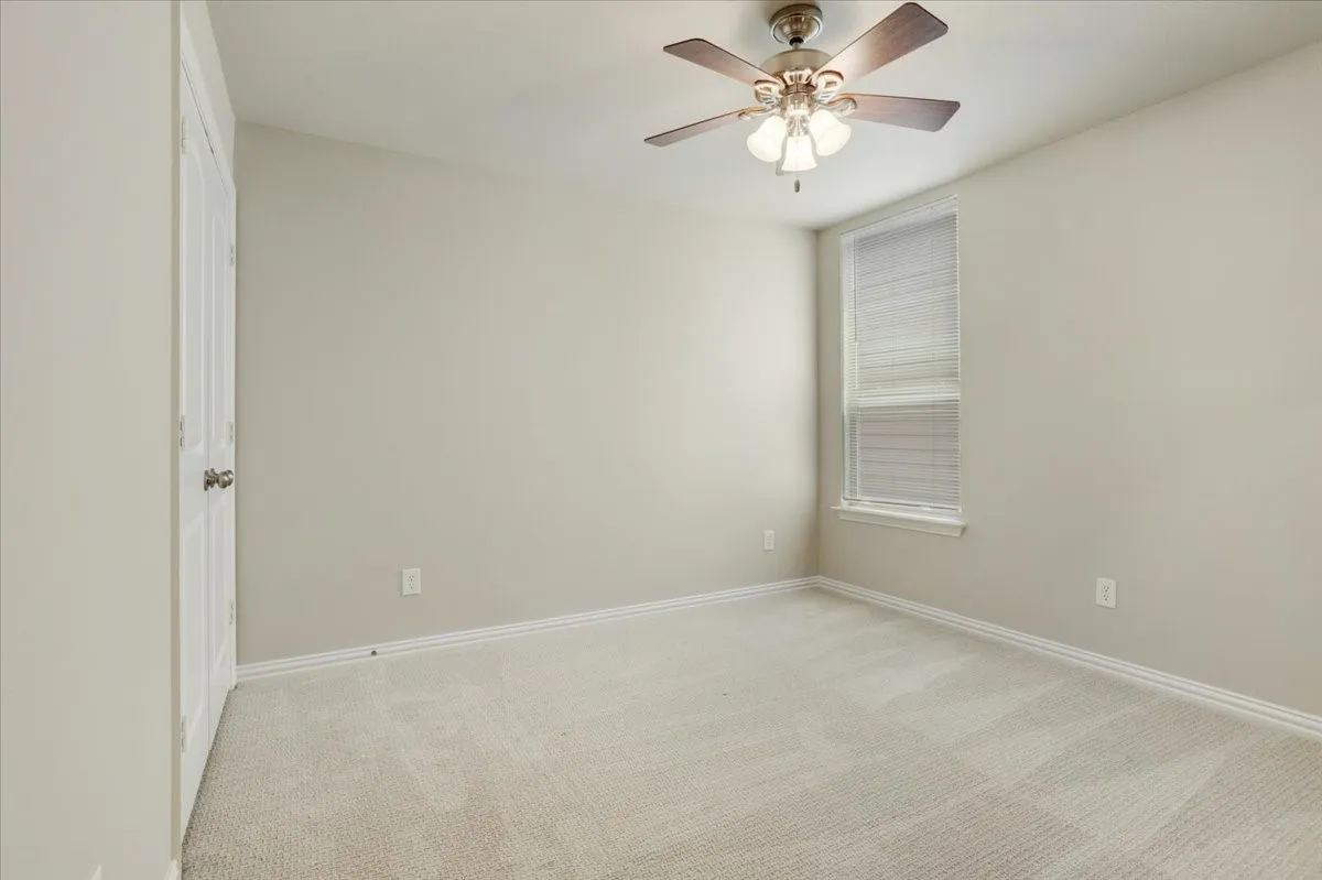 Light-colored carpeting with window featuring blinds, an overhead ceiling fan, and a white door with a round knob