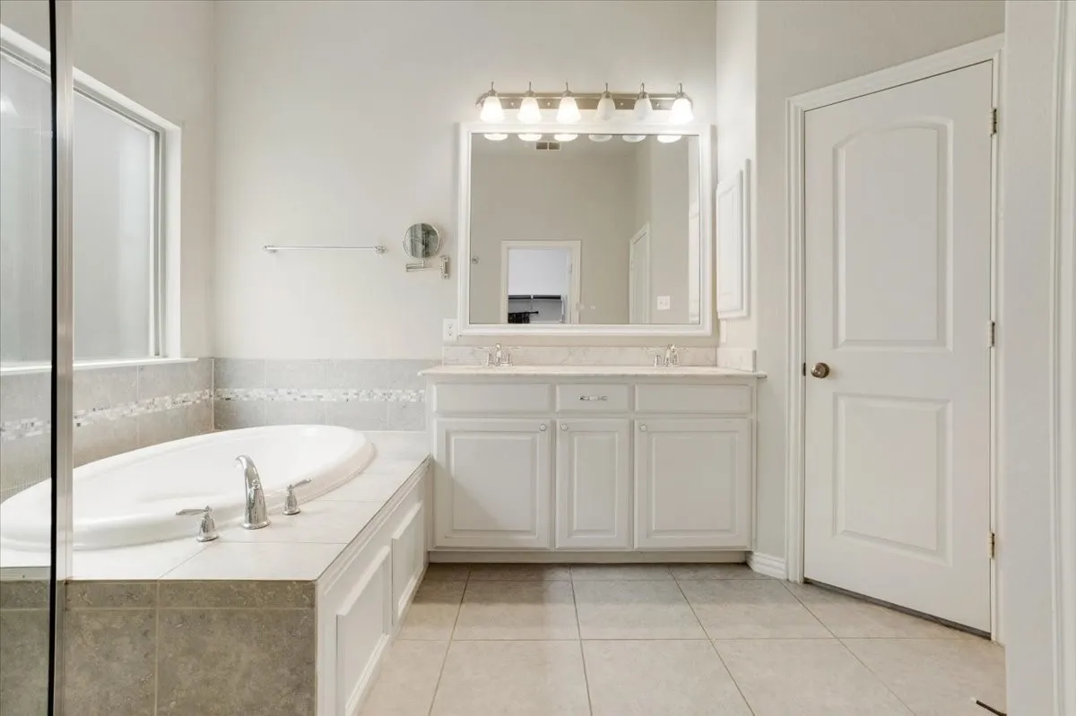 Soaking tub with deck-mounted fixtures, dual vanity with undermount sinks, and a large wall mirror