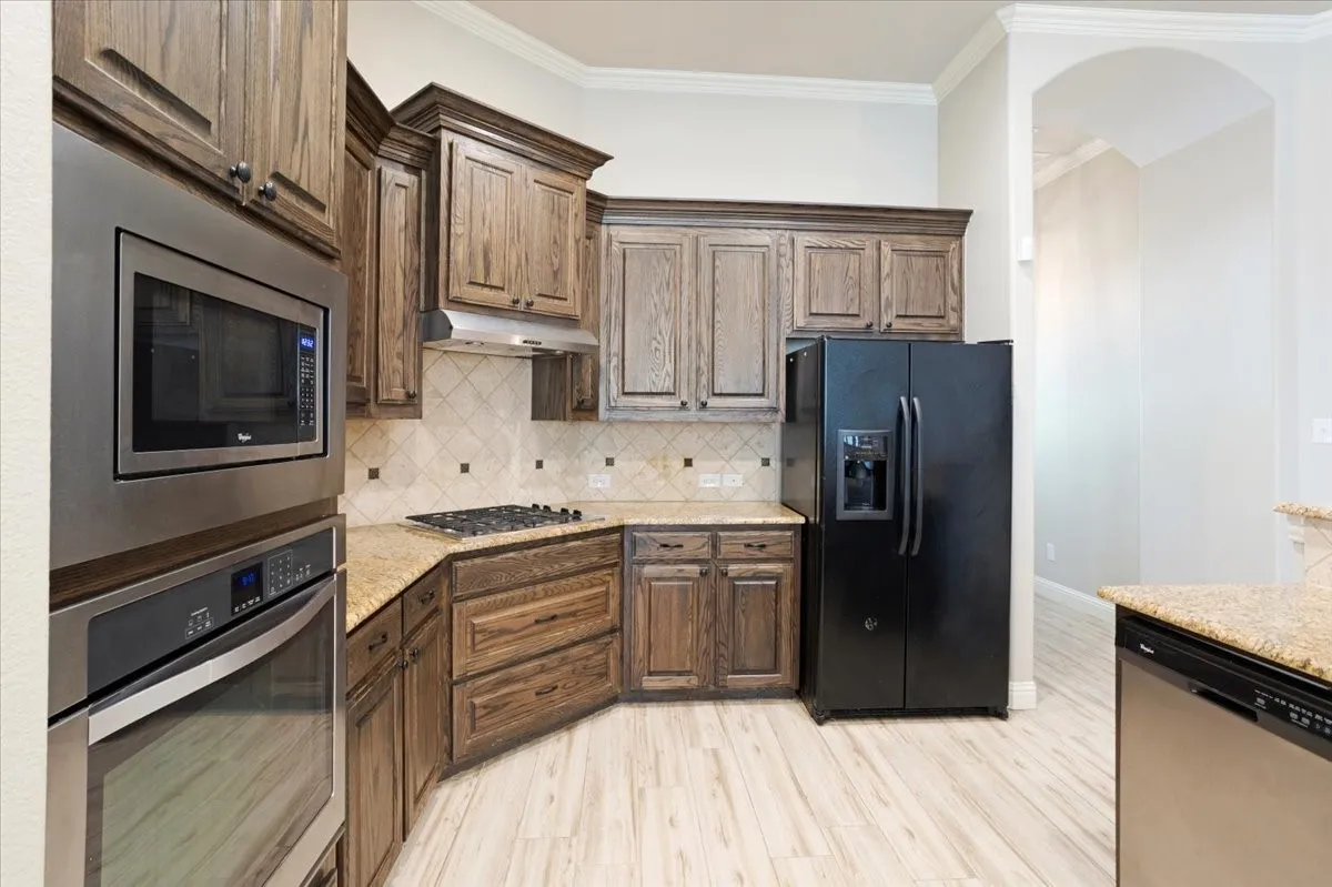 Wood-finish cabinetry, built-in stainless steel microwave and oven, gas cooktop, granite countertops, and light-toned wood-finish flooring