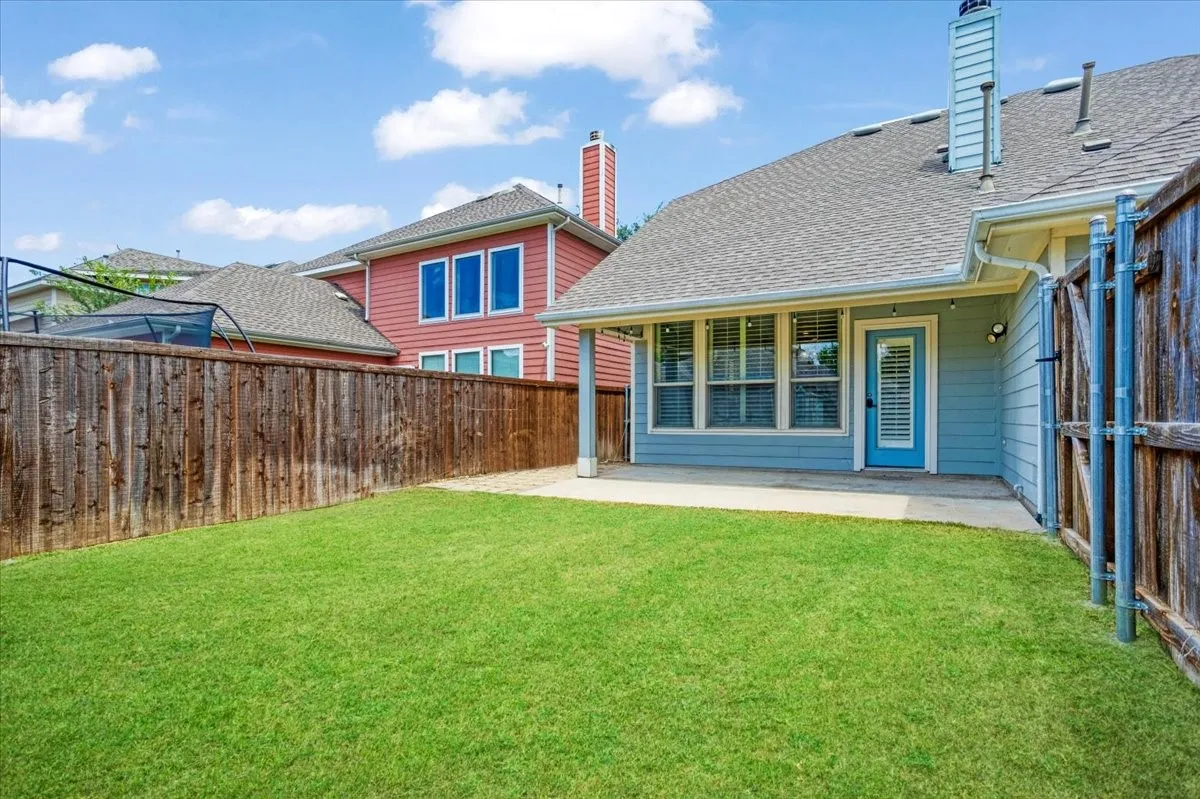 Expansive grass area with a privacy fence, concrete patio, and a light blue exterior with white trim