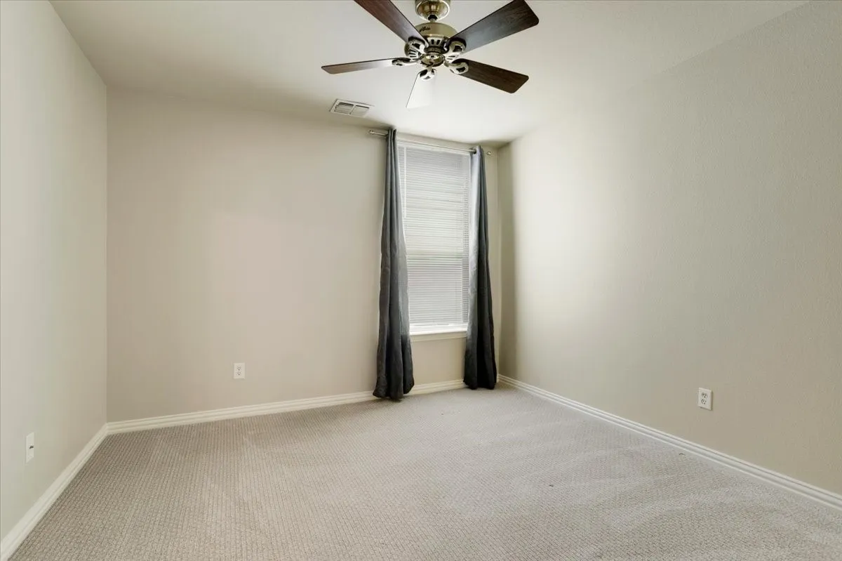 Light gray carpet flooring, neutral painted walls, ceiling fan with dark wood-finish blades, window with blinds and dark gray drapes