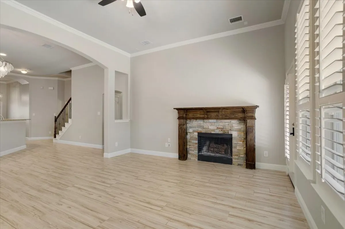 Stone-faced fireplace with a wood mantel, wood-finish flooring, plantation shutters, and an arched entryway