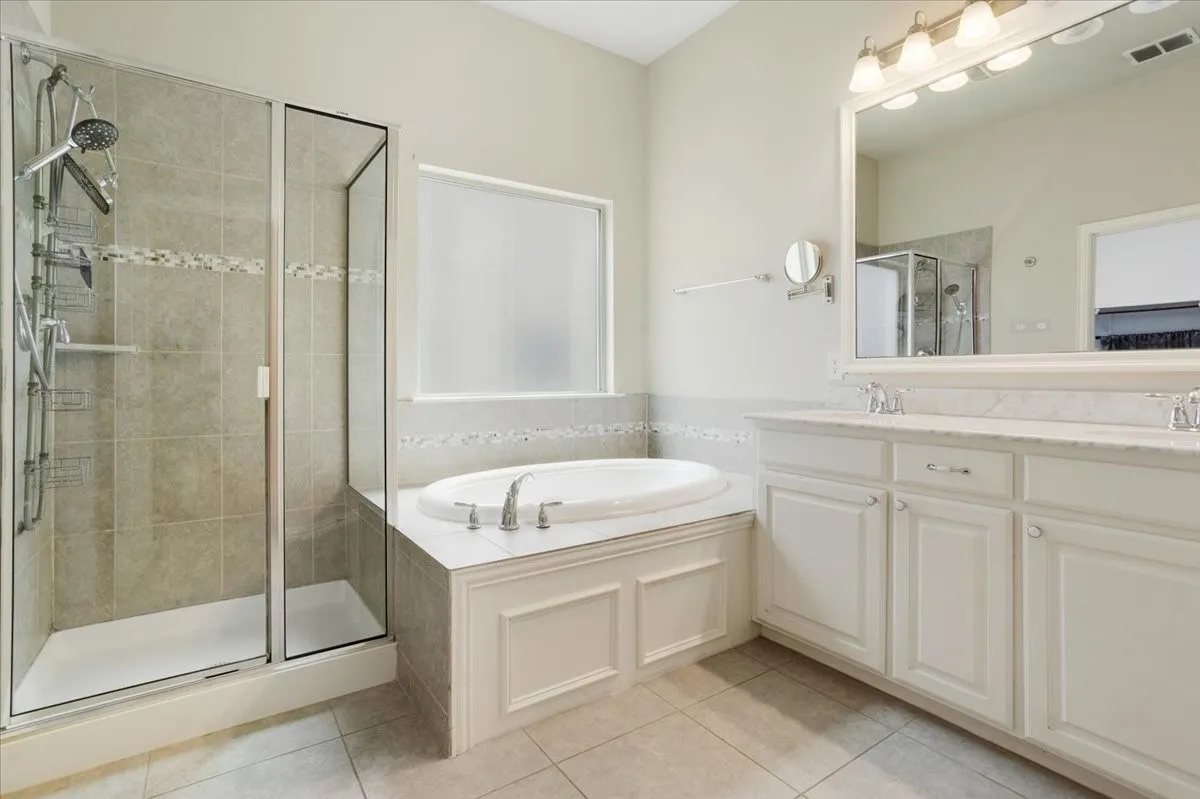 Recessed soaking tub, separate glass-enclosed shower with tile surround, dual vanity with undermount sinks, and a large wall-mounted mirror