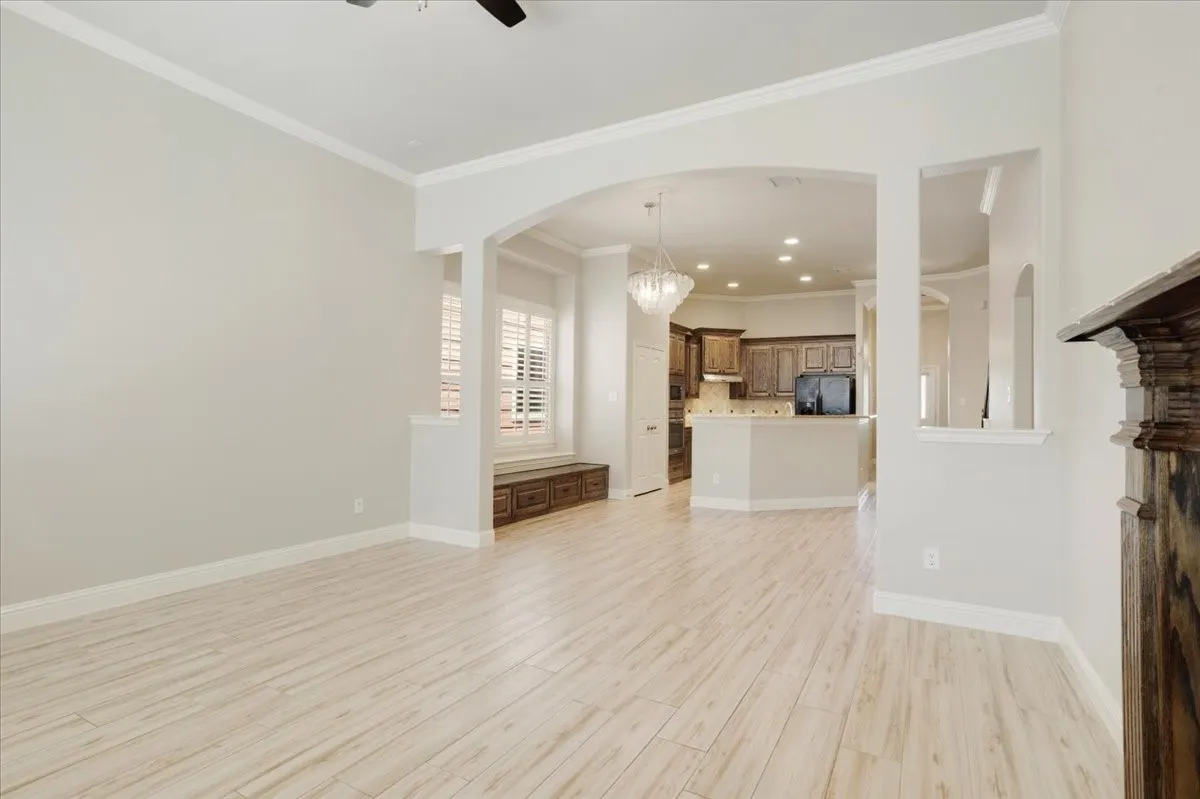 Open-concept living area featuring wood-finish flooring, an arched entryway, crown molding, and a built-in window seat with storage