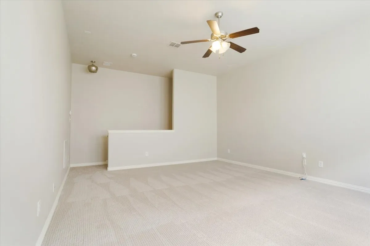 Carpeted flooring, vaulted ceiling, ceiling fan with integrated lighting, and a partial wall separating spaces