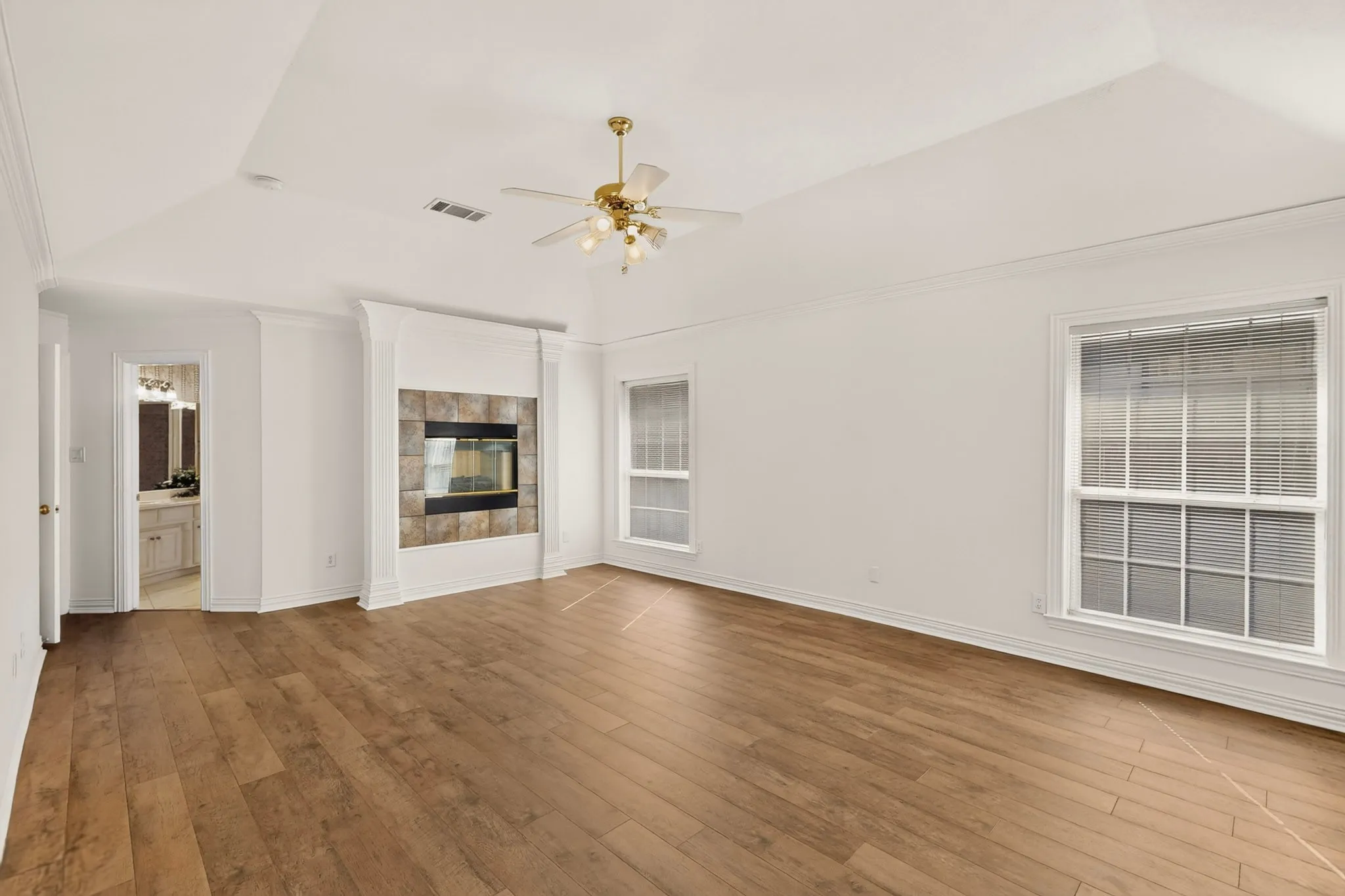 Spacious room featuring wood-finish flooring, a tray ceiling with a ceiling fan, and two large windows with blinds
