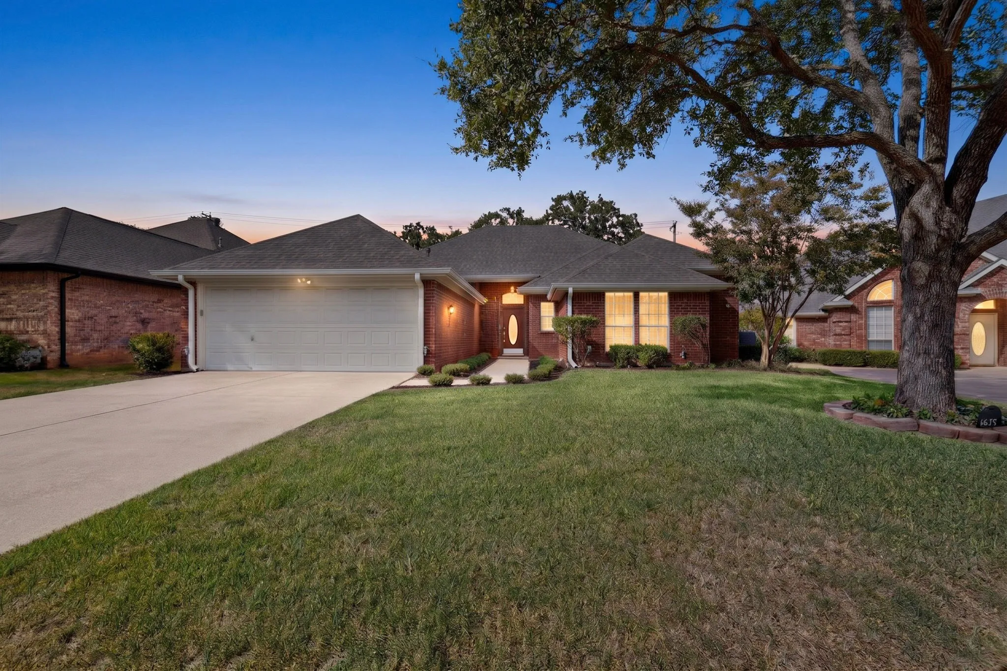 Brick exterior with an attached garage, paved driveway, and established front landscaping