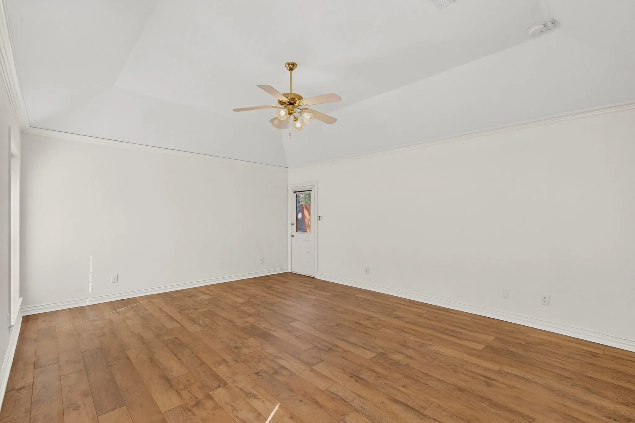 Vaulted ceiling with crown molding, wood-finish flooring, ceiling fan with light fixture, and a white door with an integrated window