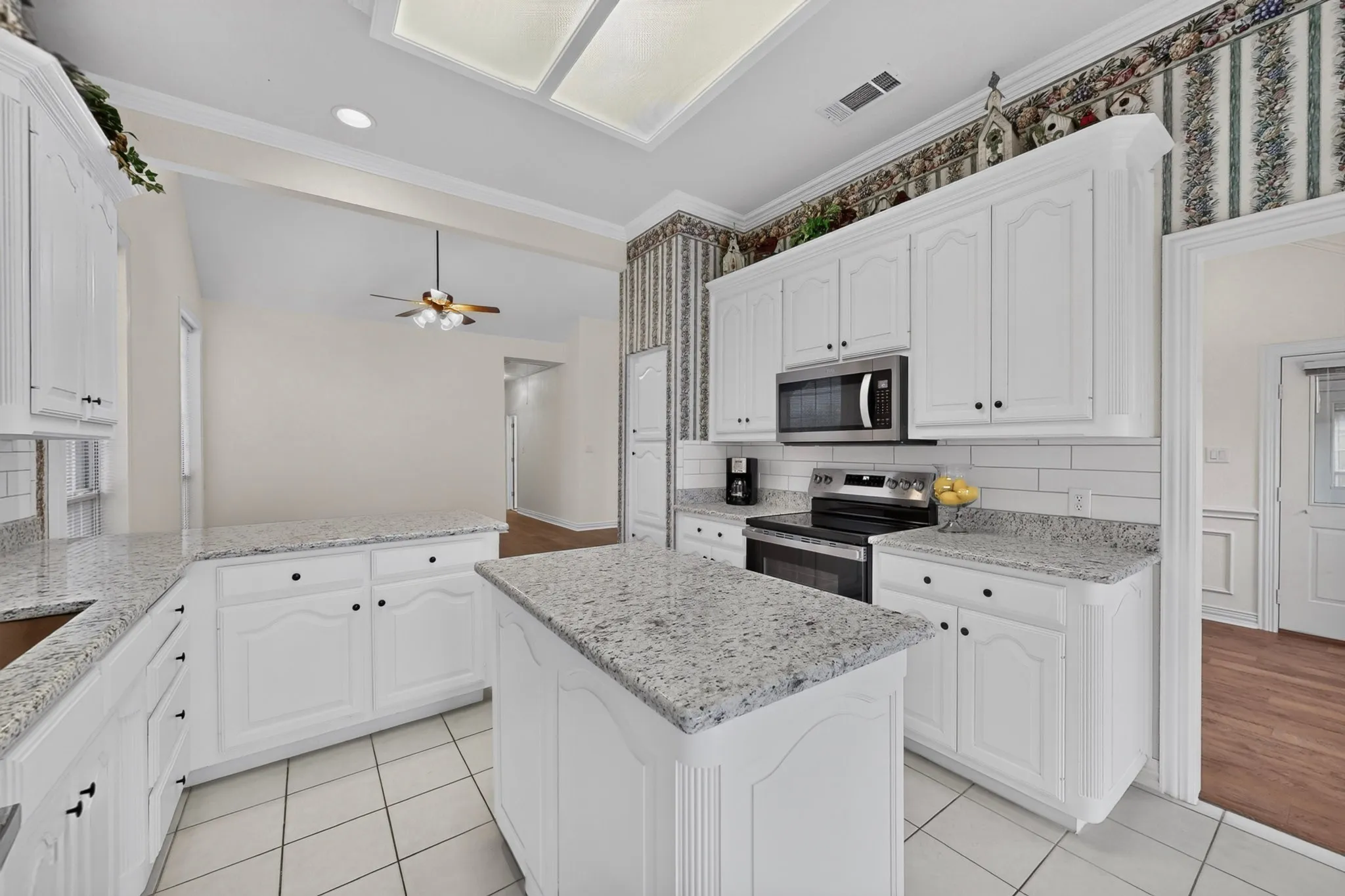 Kitchen featuring white cabinetry, granite countertops, tile flooring, a central island, and stainless steel appliances