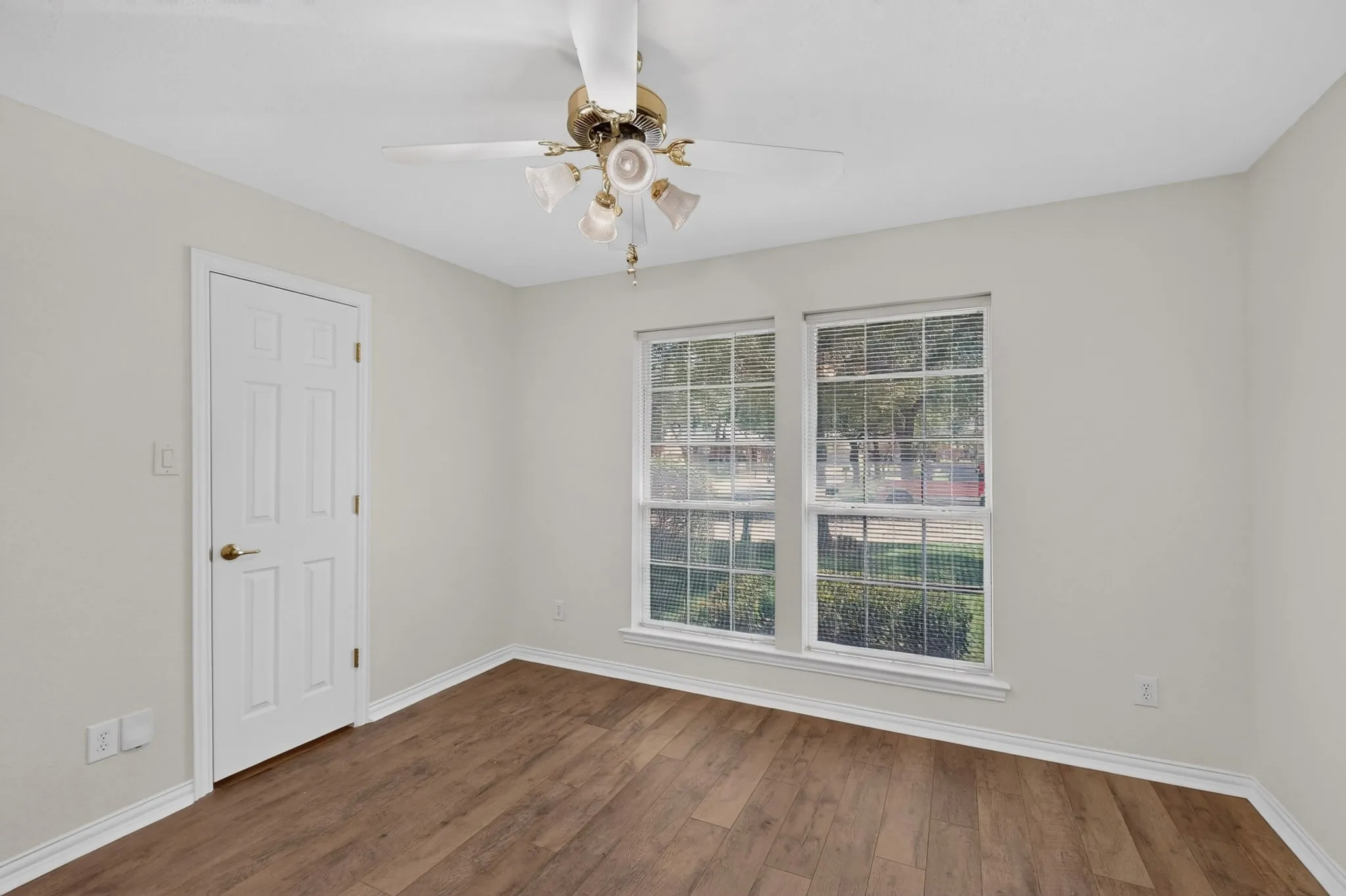 Wood-finish flooring, white walls, two windows, ceiling fan with integrated lighting, and a white paneled door