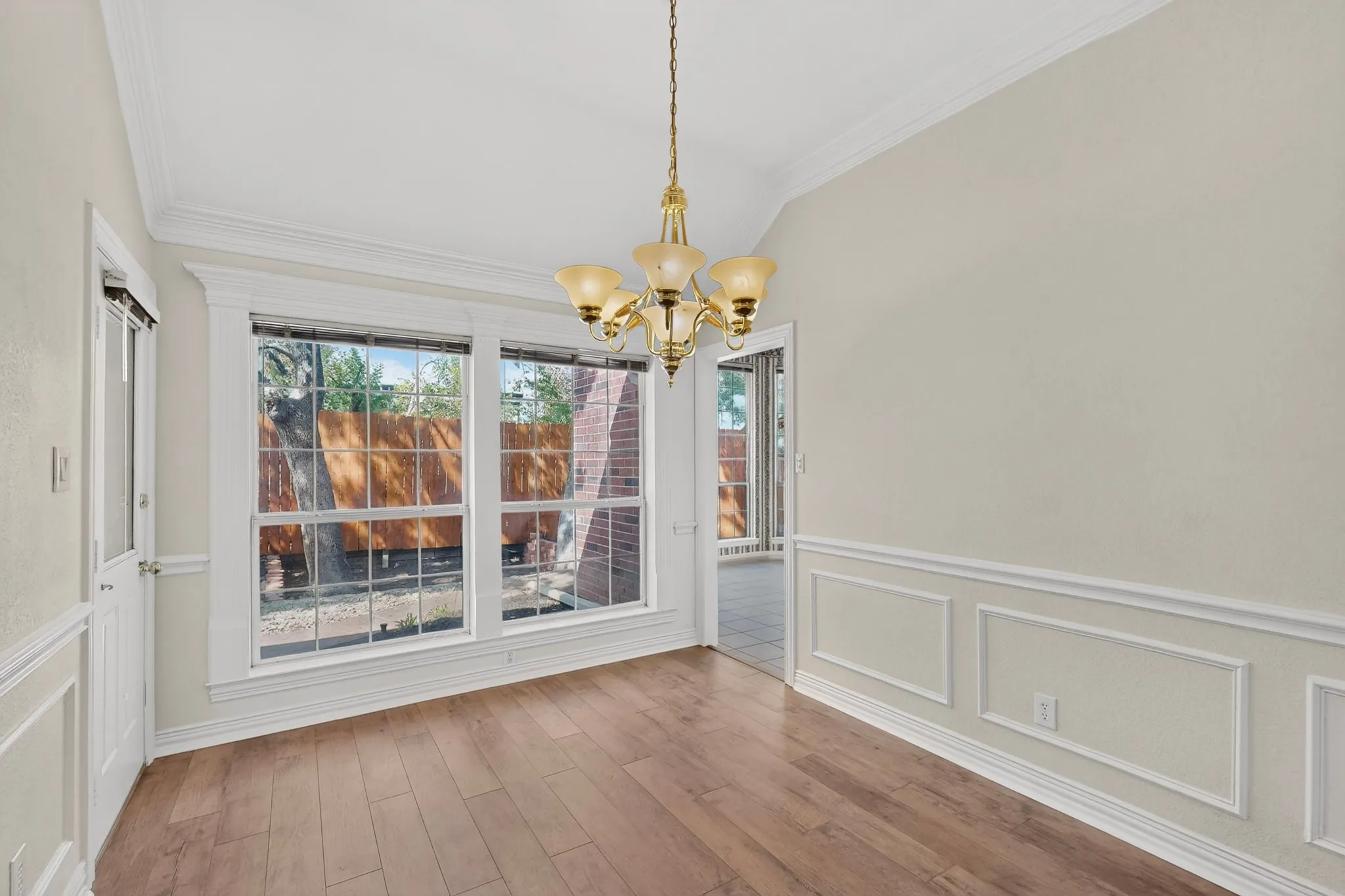 Wood-finish flooring, wainscoting details, crown molding, a multi-pane window, and an attached chandelier