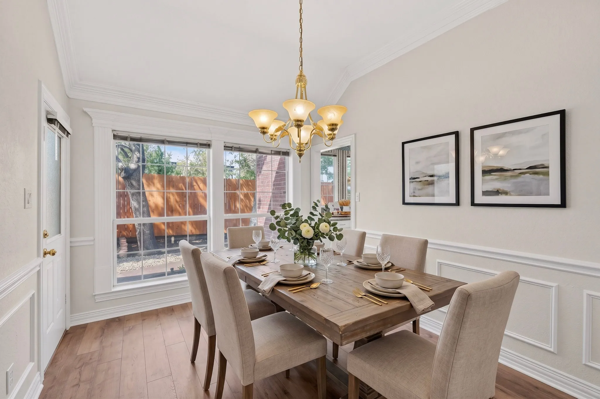 Vaulted ceiling with a brass chandelier, wood-finish flooring, large multi-pane windows, and wainscoting with decorative trim
