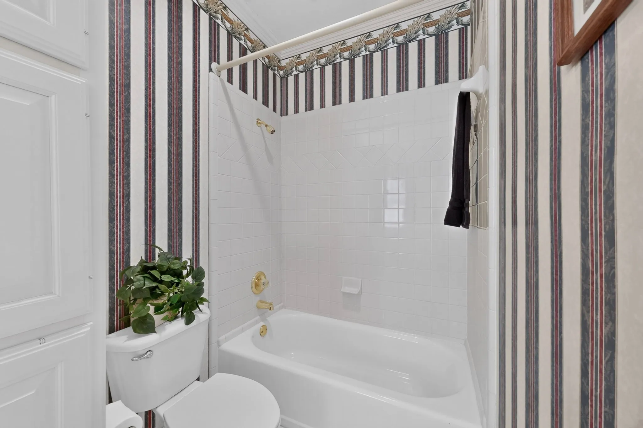 Bathtub with white tile surround, gold-finish fixtures, and a shower curtain rod