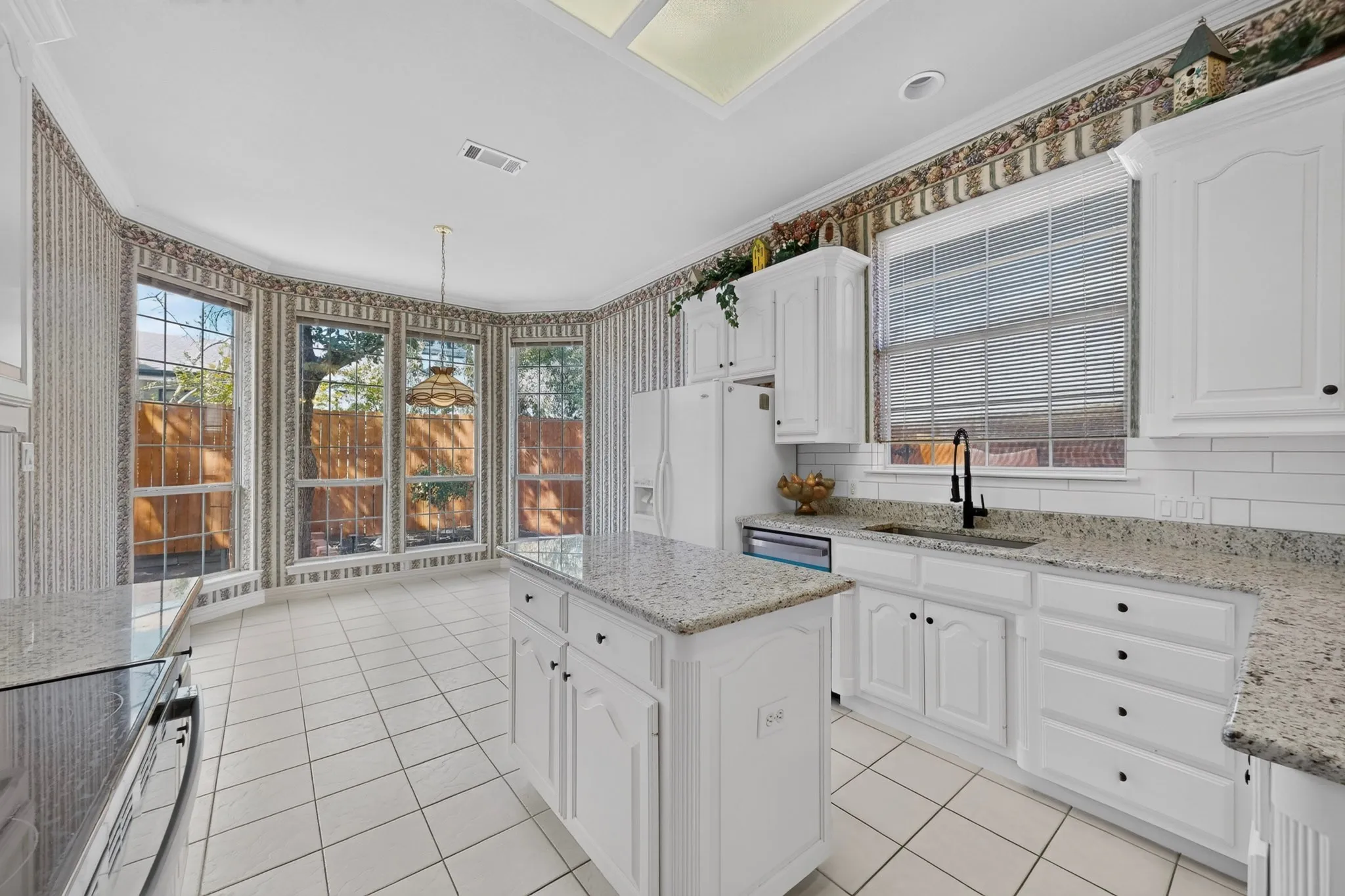 White cabinetry with black hardware, granite countertops, tile flooring, and a large bay window