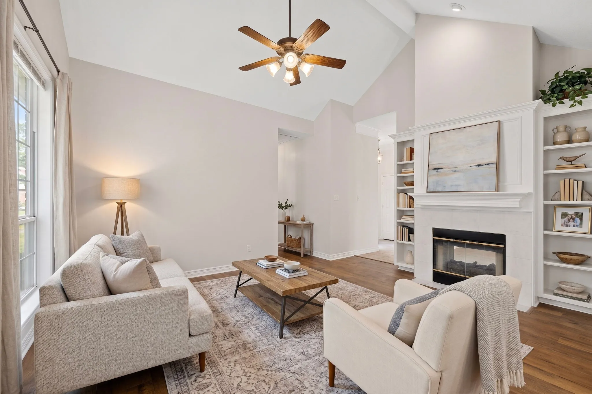 Vaulted ceiling, ceiling fan, wood-finish flooring, built-in shelving, and fireplace with mantel