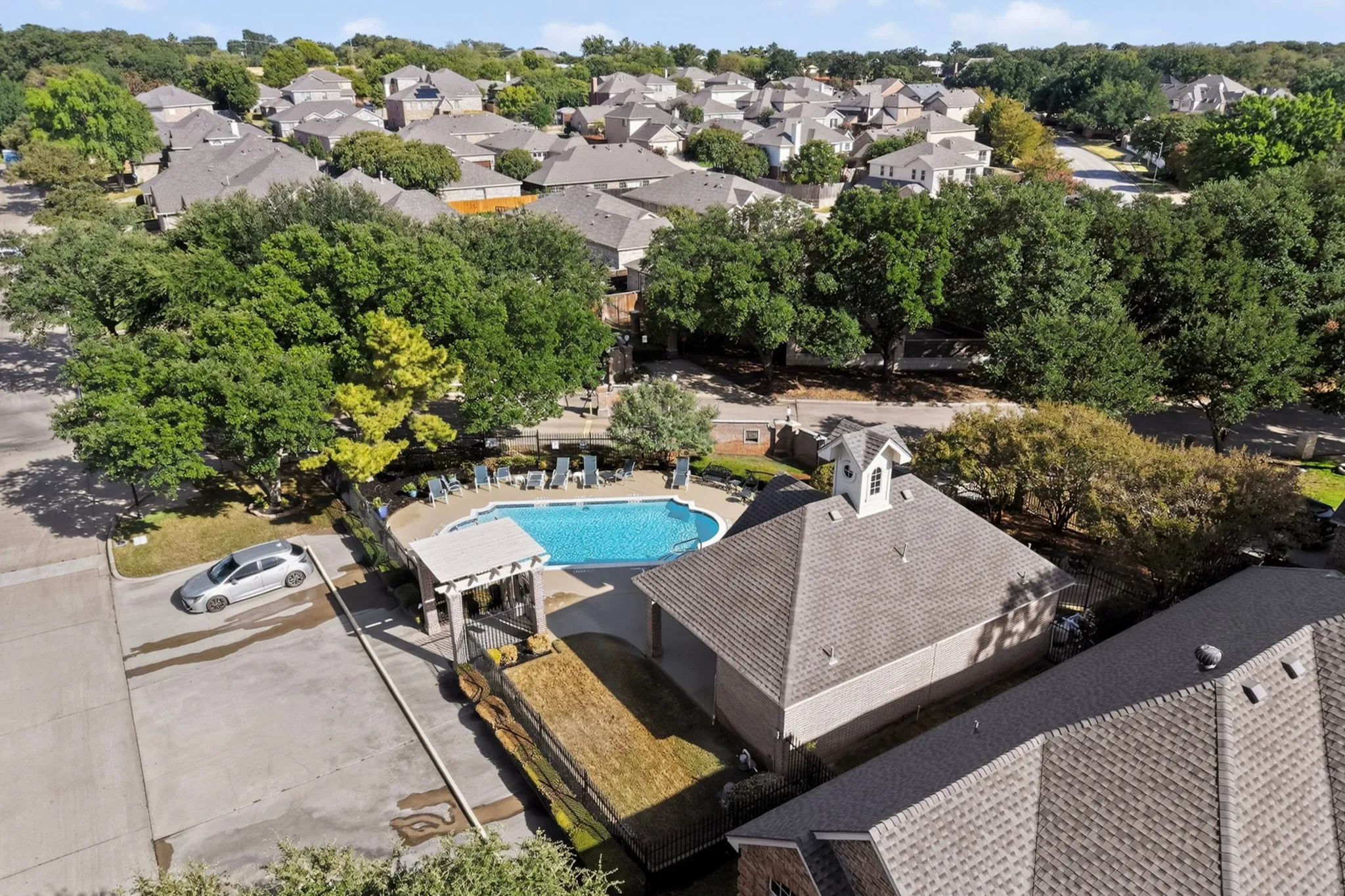 Community pool with surrounding lounge chairs, shaded pergola entry, and adjacent amenity building with cupola