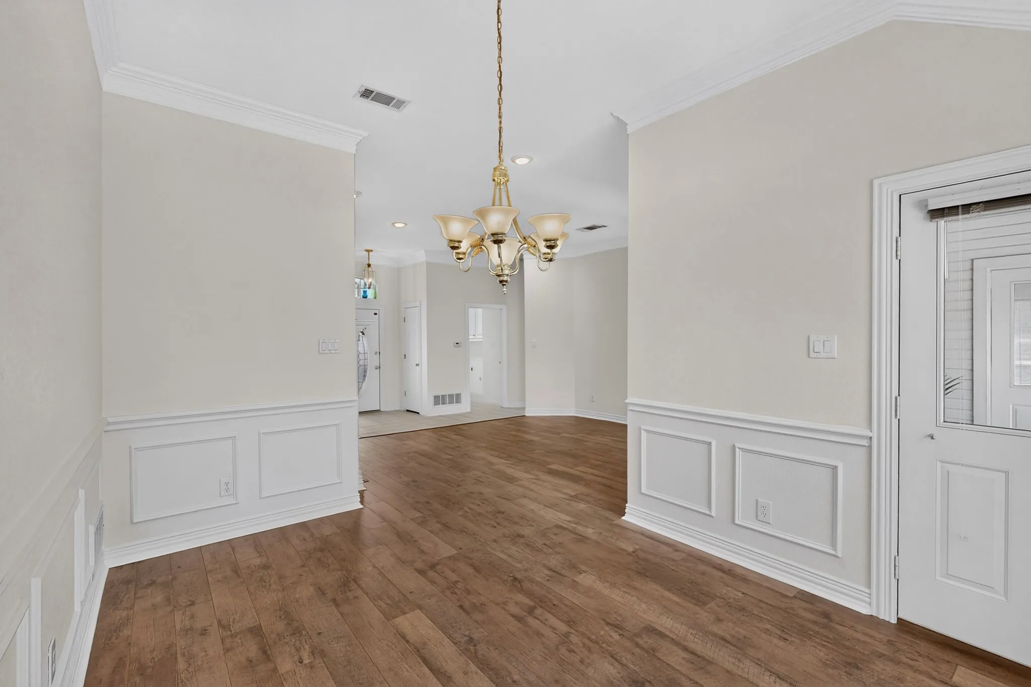 Wood-finish flooring, wainscoting, crown molding, vaulted ceilings, and a decorative chandelier