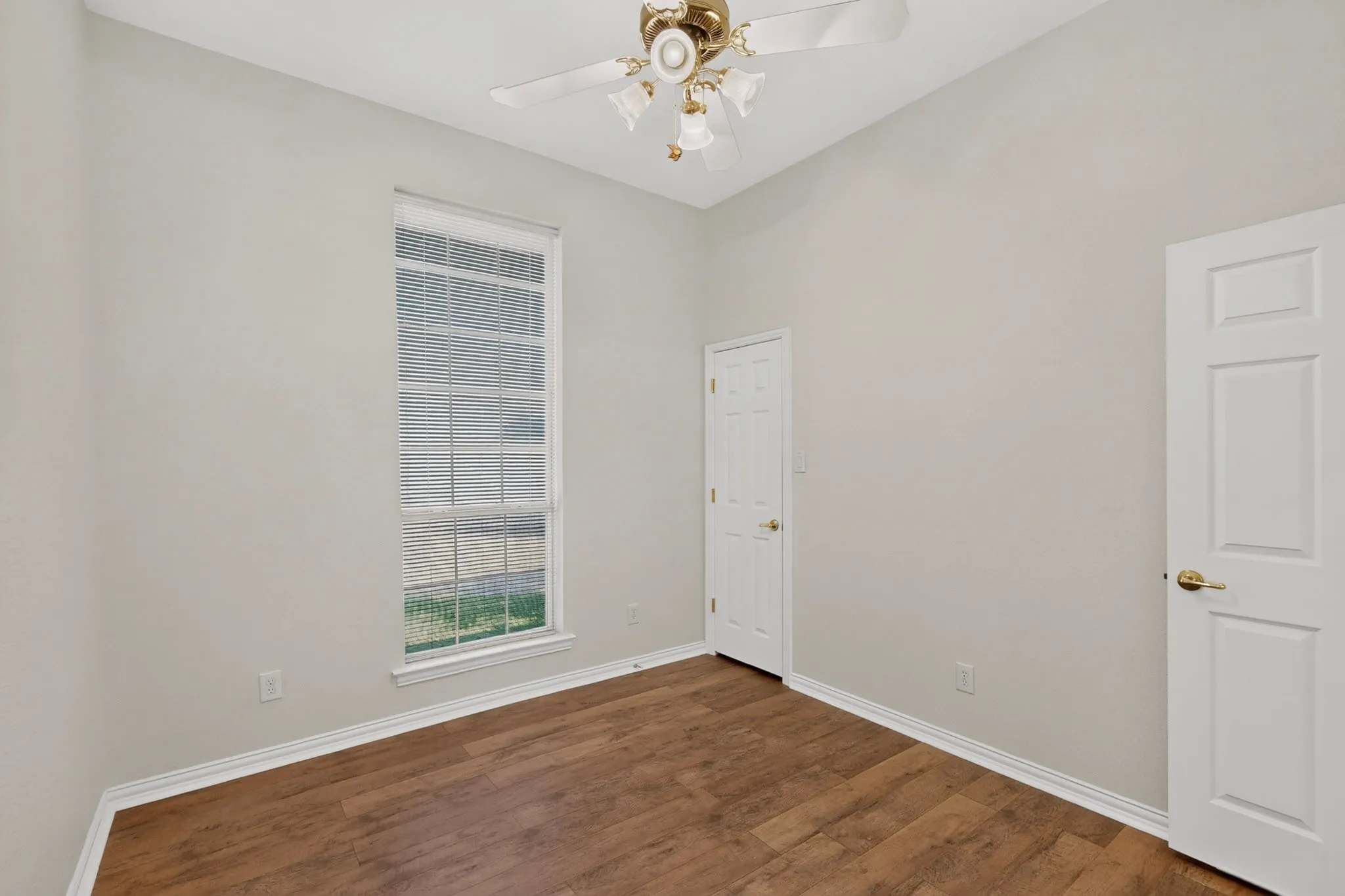 Wood-finish flooring, white trim, and a ceiling-mounted fan with integrated lighting